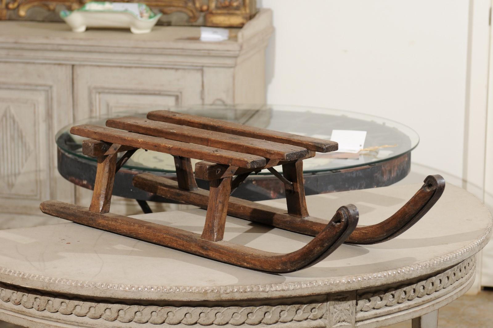 A French rustic wooden sled from the 19th century with iron braces. Charming our eyes with its rustic appearance and nicely weathered patina, this French sled features a rectangular seat made of three wooden slats resting on a curving base, ideal