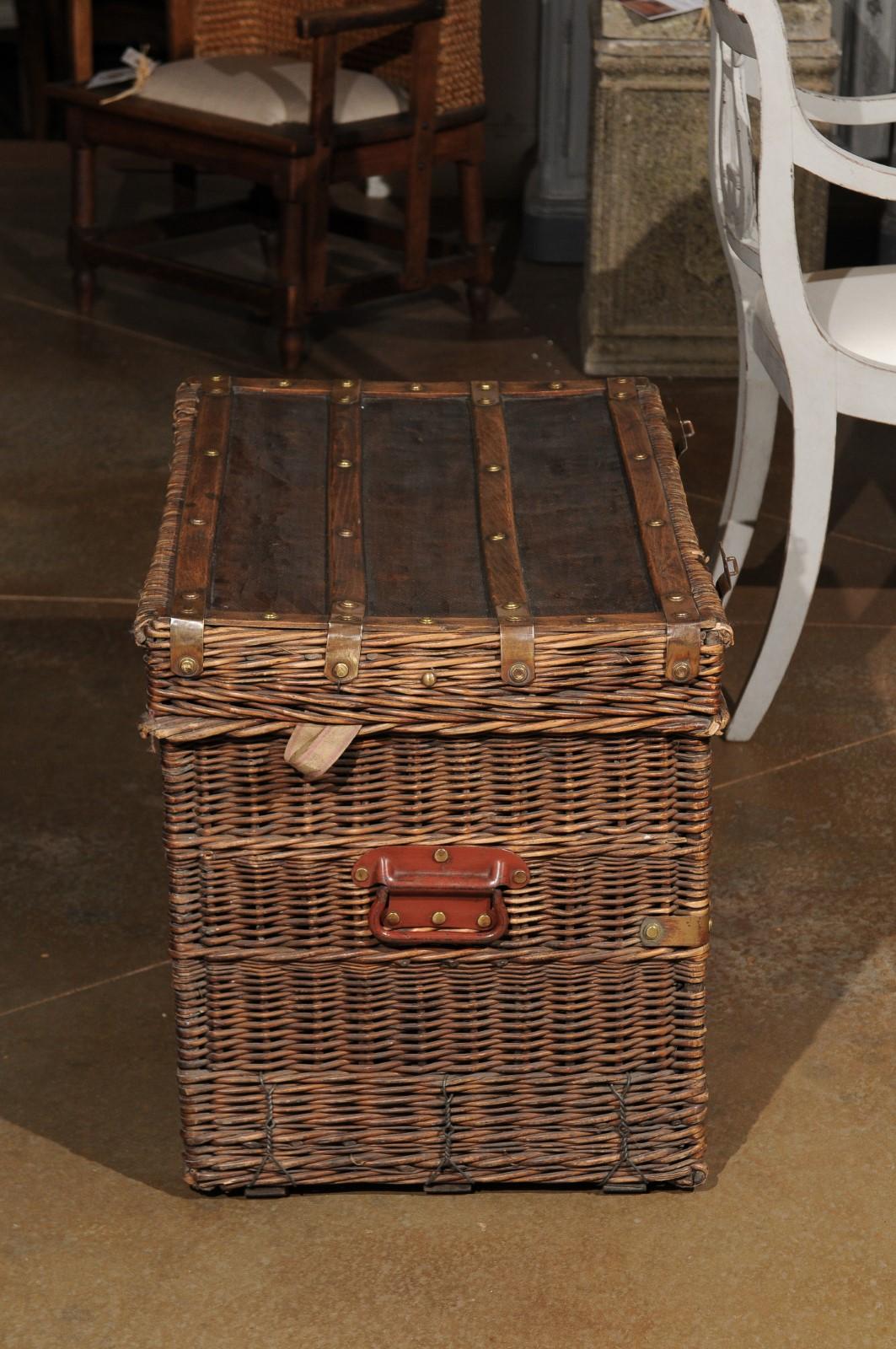 A large French wicker trunk from the 19th century, with brass hardware, straps and red painted lateral handles. Born in France during the politically dynamic 19th century, this wicker trunk features a rectangular lid, adorned with straps, opening