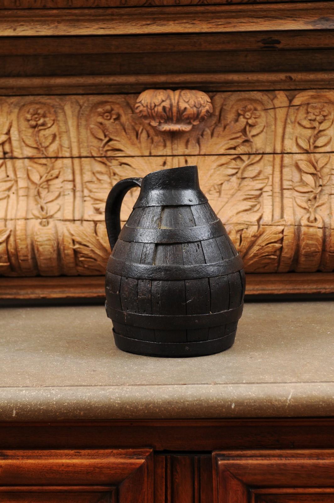 A French rustic wine jug from the 19th century, with dark patina. Created in France during the 19th century, this wine jug charms us with its rustic appeal and dark patina. Made of a succession of vertical wooden slats strengthened by metal braces,