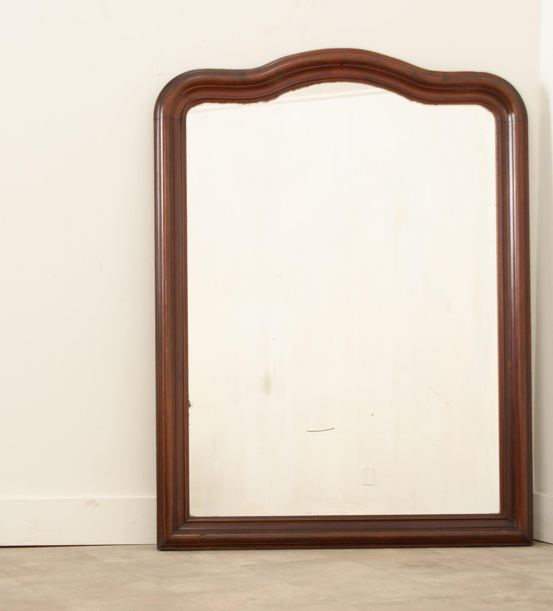 A beautifully shaped  French wall or mantel mirror made of walnut and hand-crafted in France in the 19th century.  This elegant mirror features a fine sculptural design with flowing shapes and lines. The molded wood frame is a rich brown color and