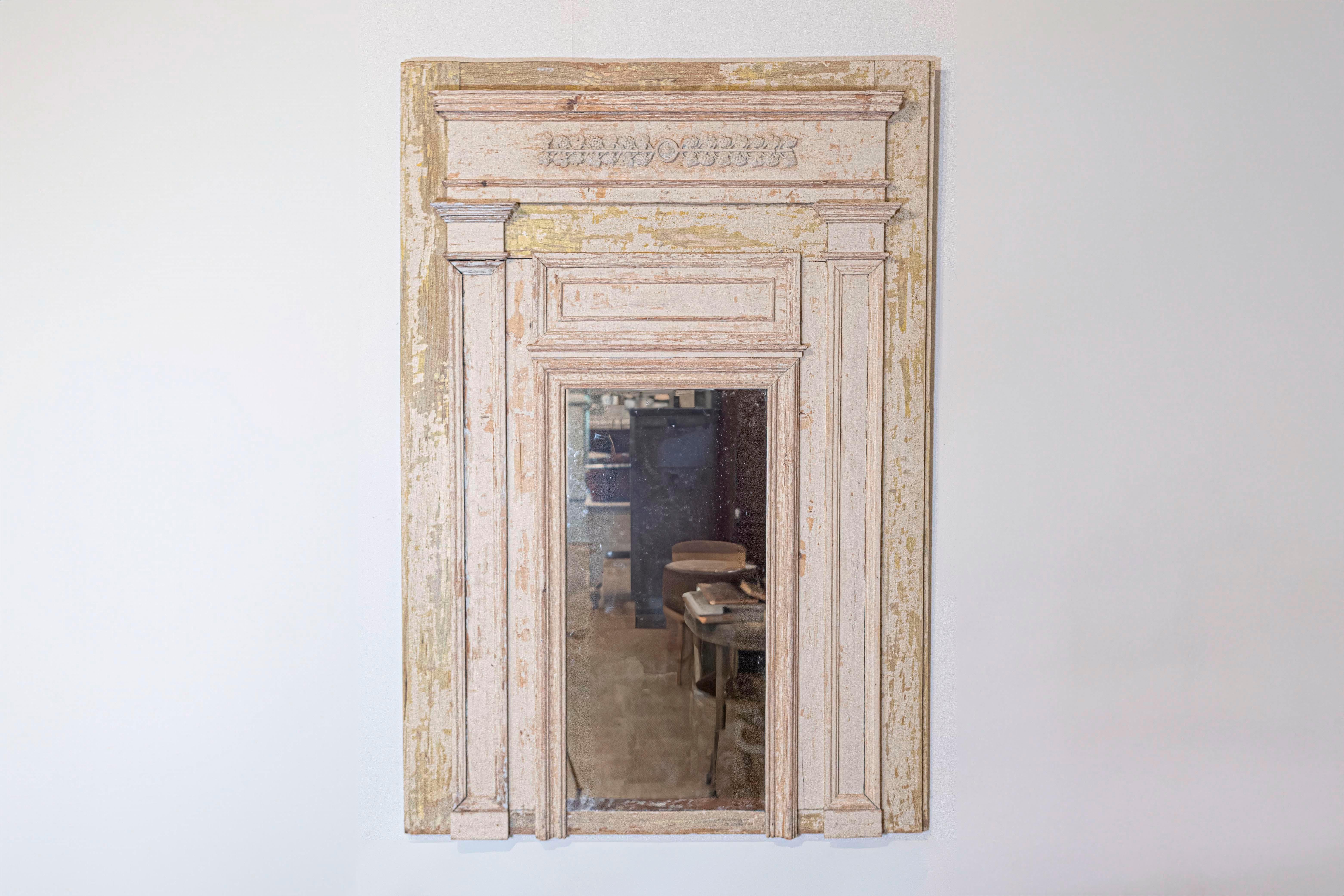 A French scraped wooden trumeau mirror from the 19th century, with carved grapes and Doric pilasters. Created in France during the 19th century, this trumeau mirror features a scraped background adorned with a portico style structure. The lintel is