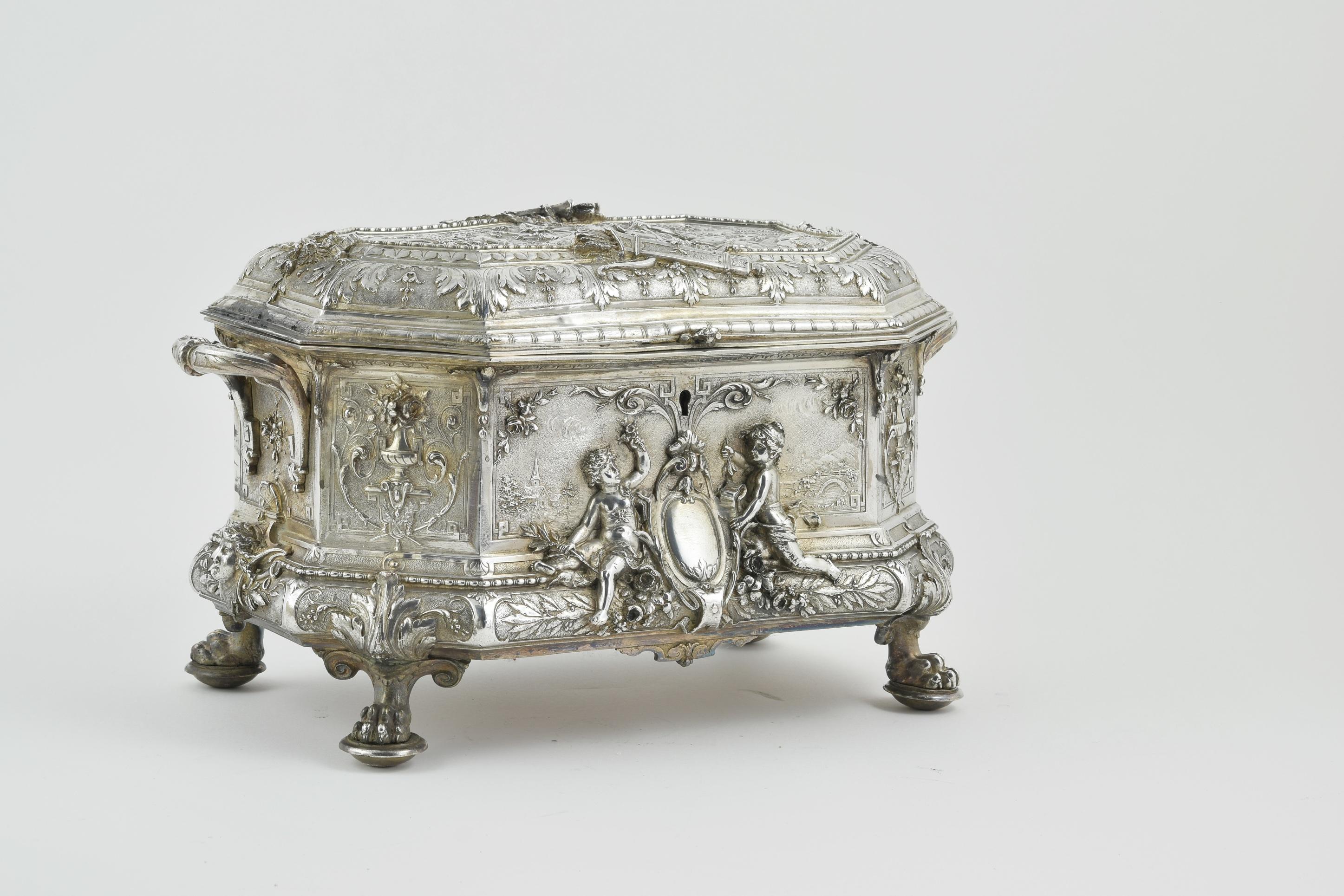 The whole casket is richly decorated. Standing on lions paw feet adorned with baroque motifs the scene on top depicts cupid stood beside two lovers (possibly) Daphne and Apollo. The front and rear of casket with empty shield flanked by cherubs.