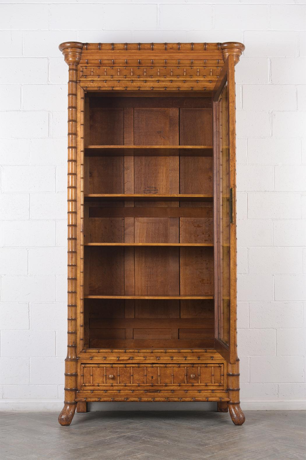 This 1850s French one door bamboo bookcase is made out of birch, bamboo, and oak wood combination with the original stained color, and has a beautiful natural patina finish. The bookcase has carved moldings around the corners of the crown and feet.