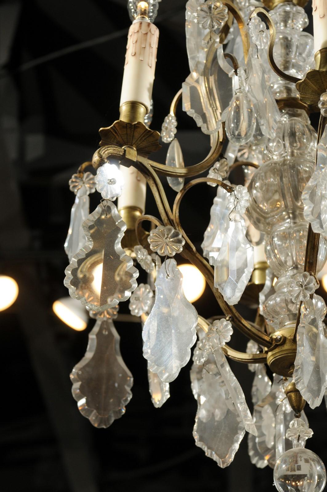 A French six-light bronze and crystal chandelier from the 19th century, with scrolling arms and flower-shaped bobèches. Born in France during the politically dynamic 19th century, this exquisite chandelier features a bronze armature draped with