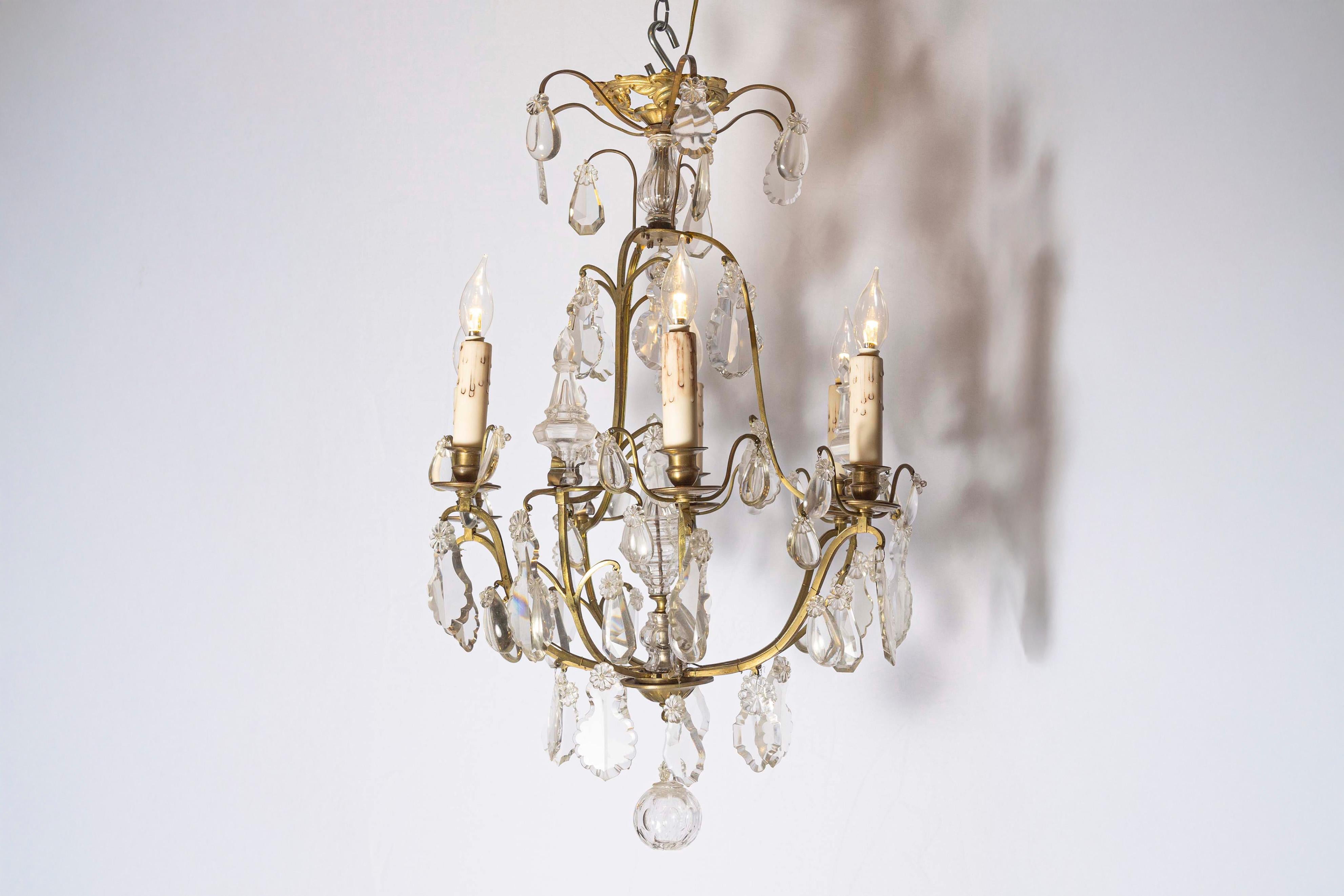 A French six-light crystal chandelier from the 19th century, with brass armature, pendeloques and round finial. Born in France during the politically dynamic 19th century, this lovely six-light chandelier features a scrolled brass armature, draped