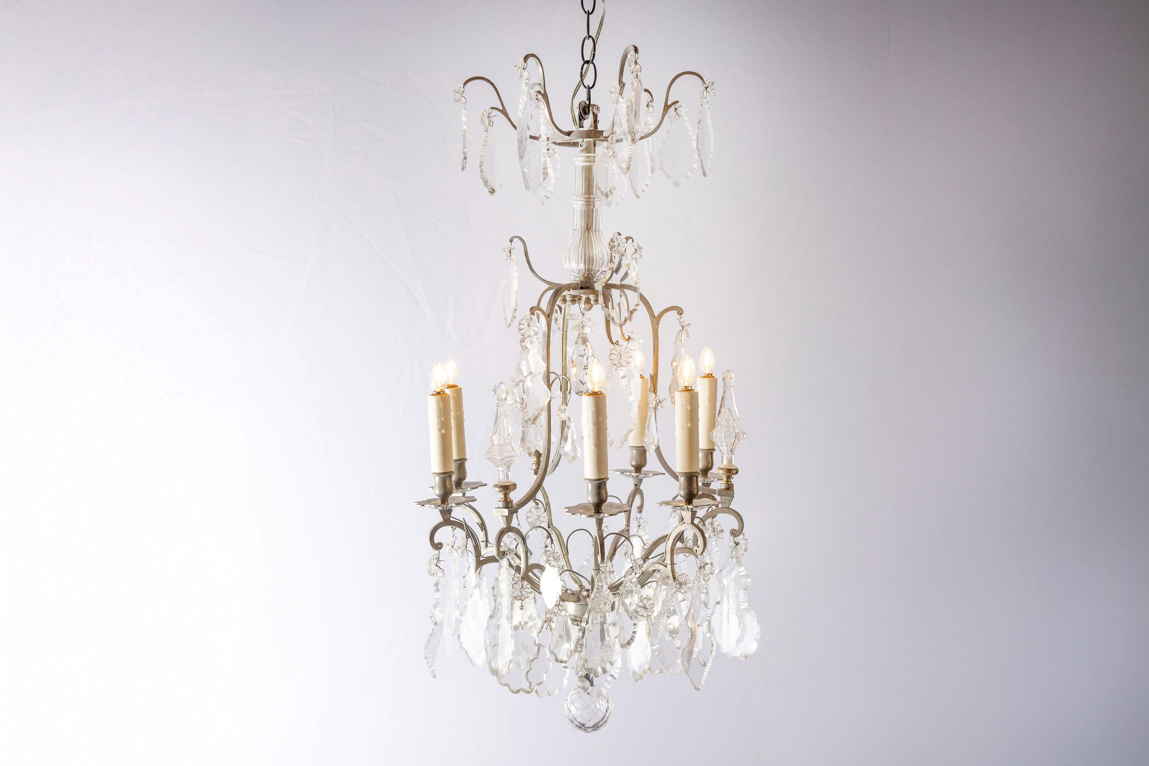 A French six-light crystal chandelier from the 19th century, with silvered iron armature. Born in France during the 19th century, this exquisite chandelier presents a tiered Silhouette made of silvered iron scrolls adorned with pendeloques, leading