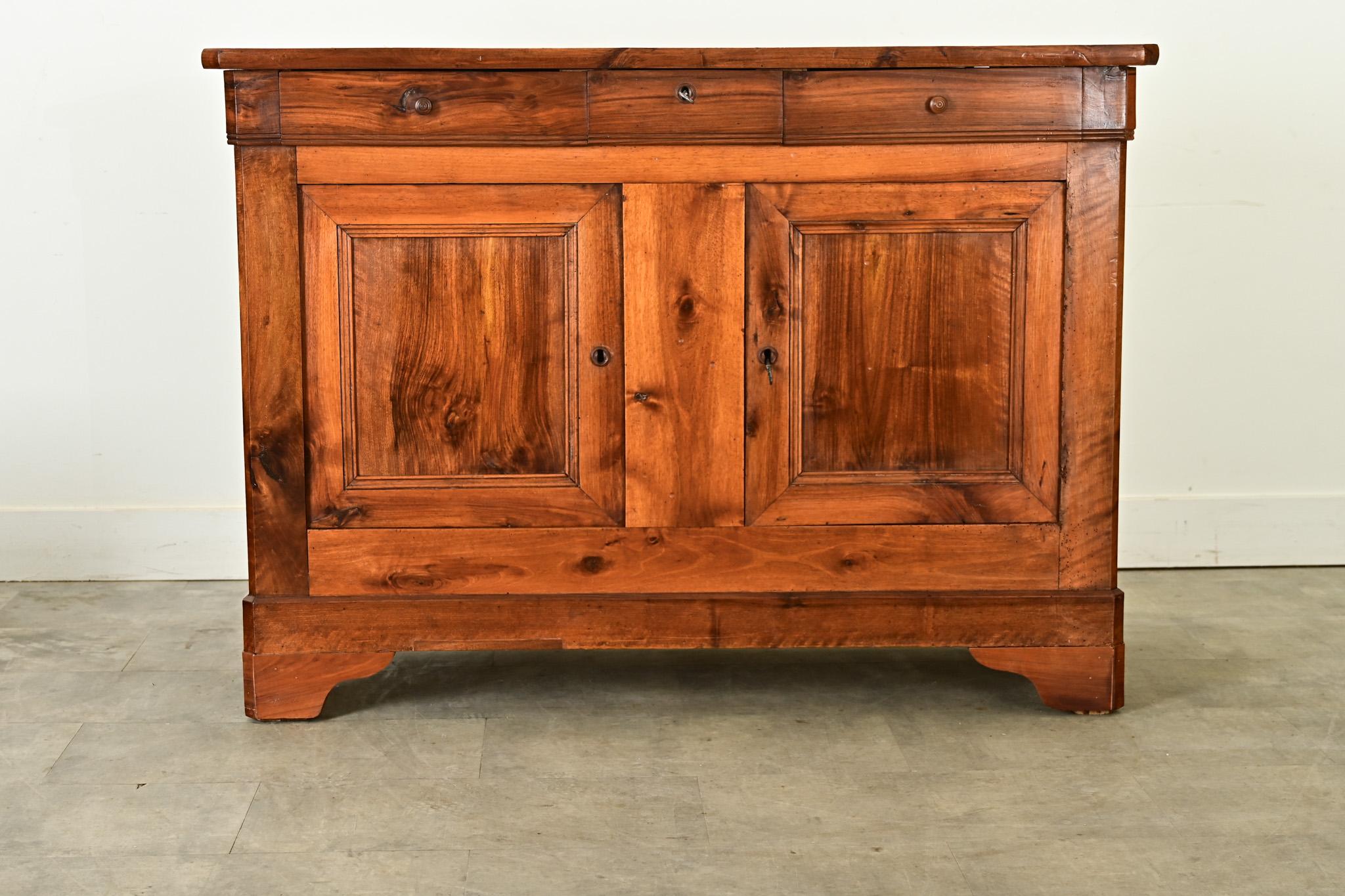 Questo bellissimo buffet in legno di frutta in stile Louis Philippe del XIX secolo si distingue per le luminose tonalità del legno e le venature delle ante e dei cassetti. Le tavole superiori hanno una consistenza morbida che completa il colore