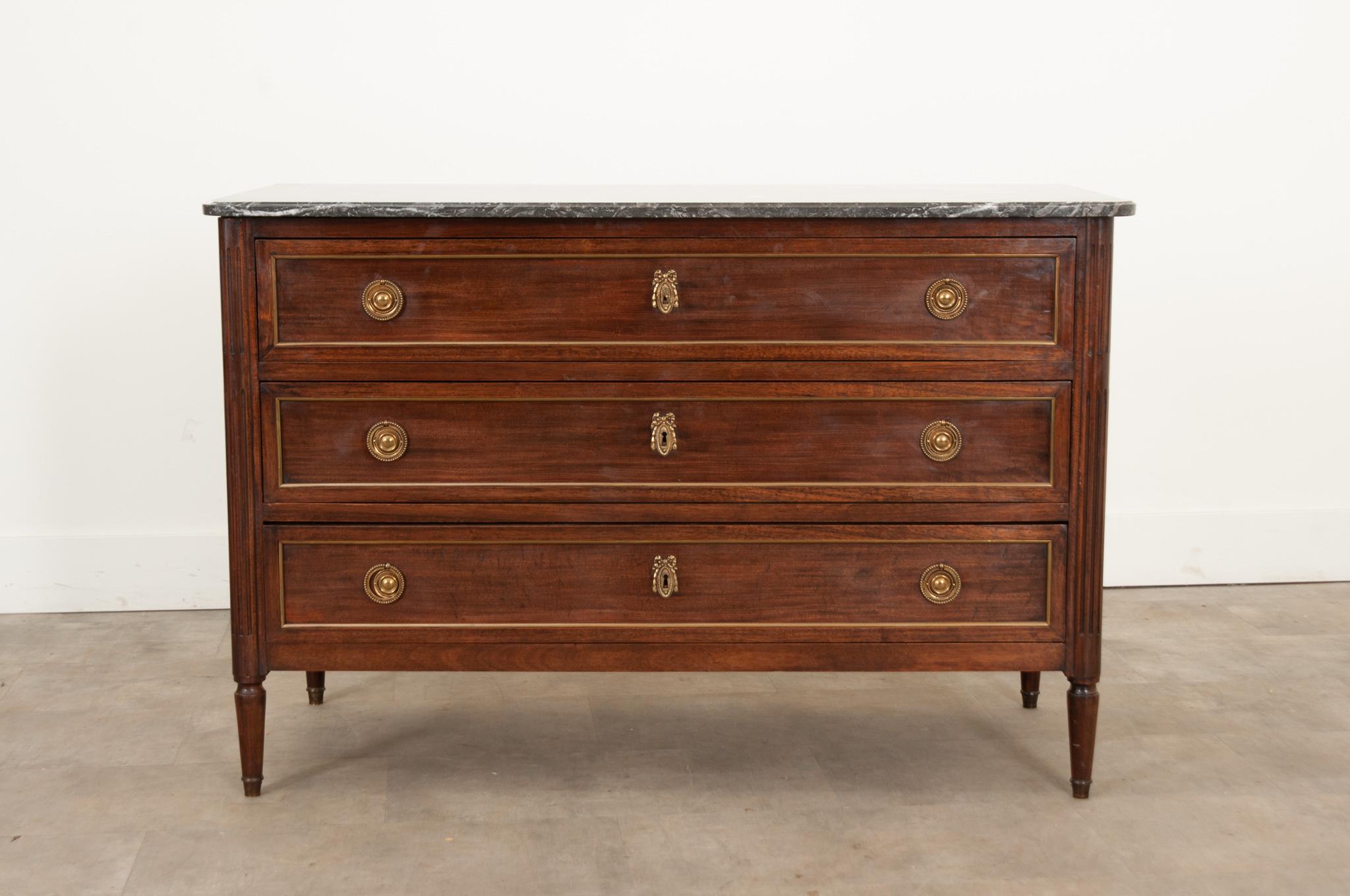 A French 19th century commode that was hand-crafted in France during the 19th century, circa 1830. This case piece features its original shaped marble top, three wide drawers with elaborate beribboned and bellflower escutcheon plates and round brass