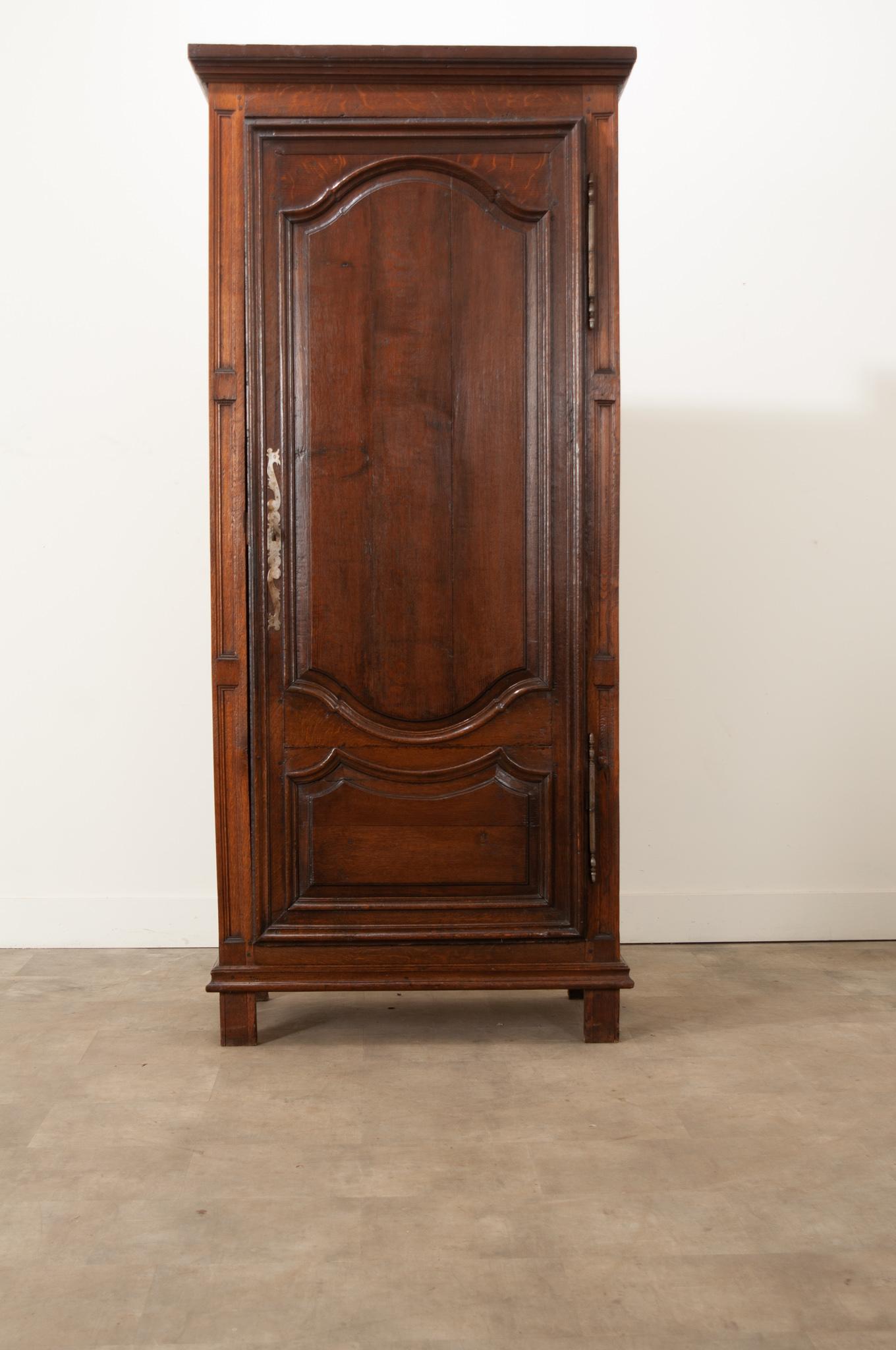 This lovely antique bonnetiere, made of solid oak of varying tones and textures, was carved and constructed in 18th century France, circa 1750. This wonderful cabinet features a single tall door that closes before its interior. The door is decorated