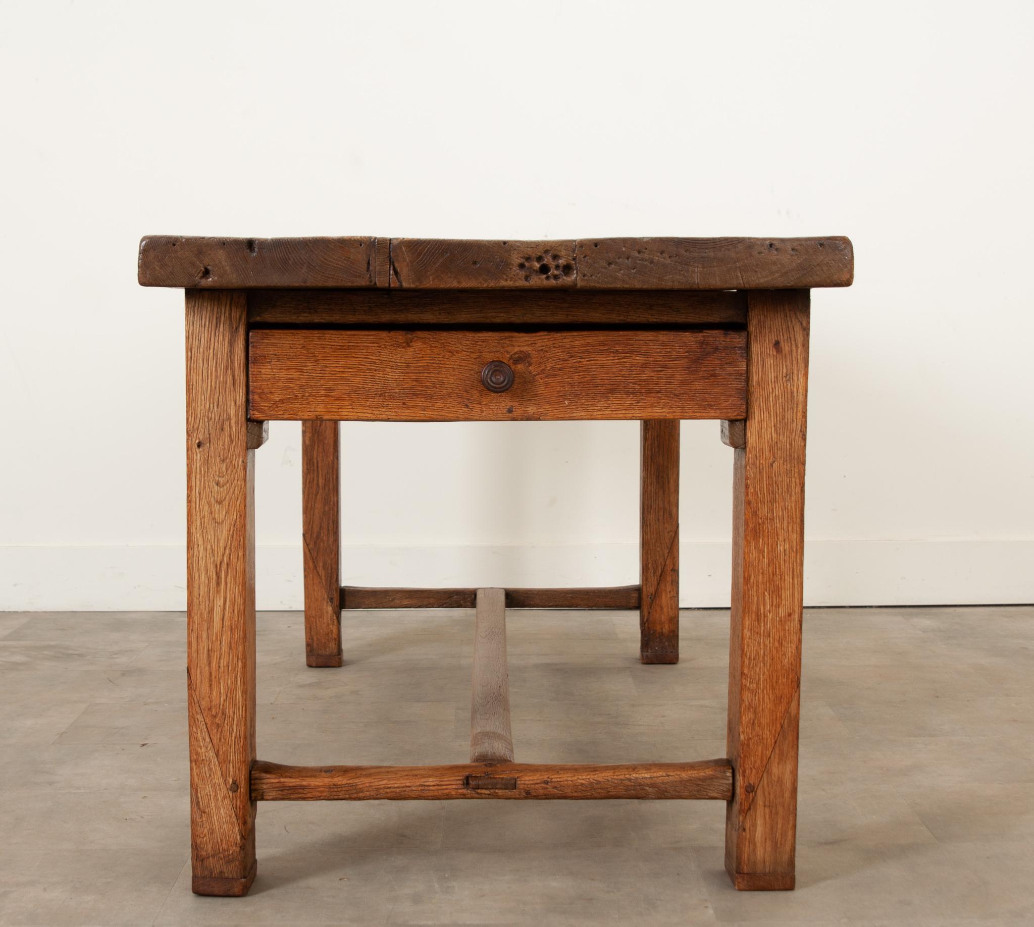 This primitive solid oak farmhouse table is sound and sturdy with a handsome patina. The two board 2” thick top sits over study block legs connected with an apron and stretcher base. There are two long drawers found in the apron that pull from each