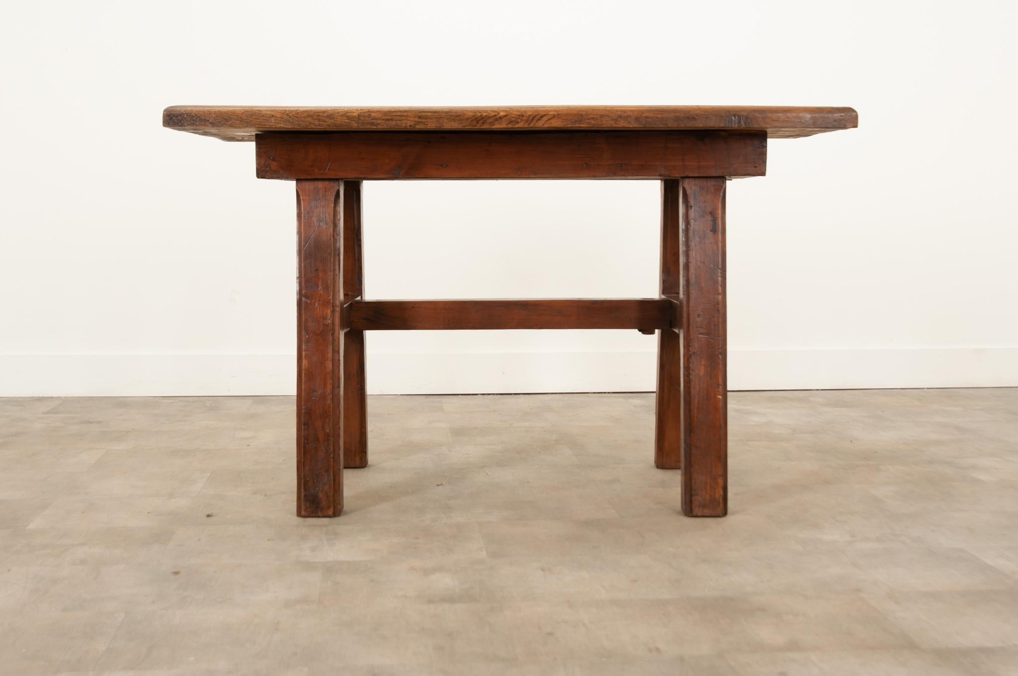 A robust French 19th century solid oak work table handcrafted in France circa 1870. The two inch thick top is made up of five planks with a molded and trimmed edge that overhangs a simple apron supported by thick A-framed and decoratively chamfered