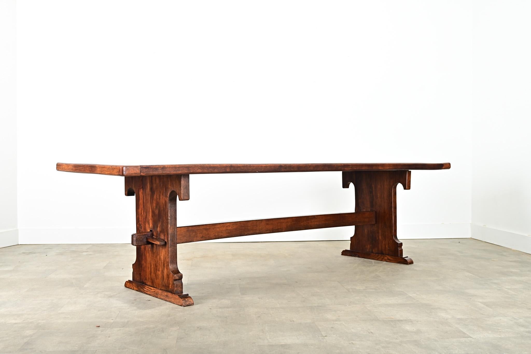 A monumental 19th century French oak dining table with unique decorative elements in the trestle base. Impossibly heavy, the top planks are 2” thick old-growth wood including dense grain patterns and knots left by the pre-industrial milling
