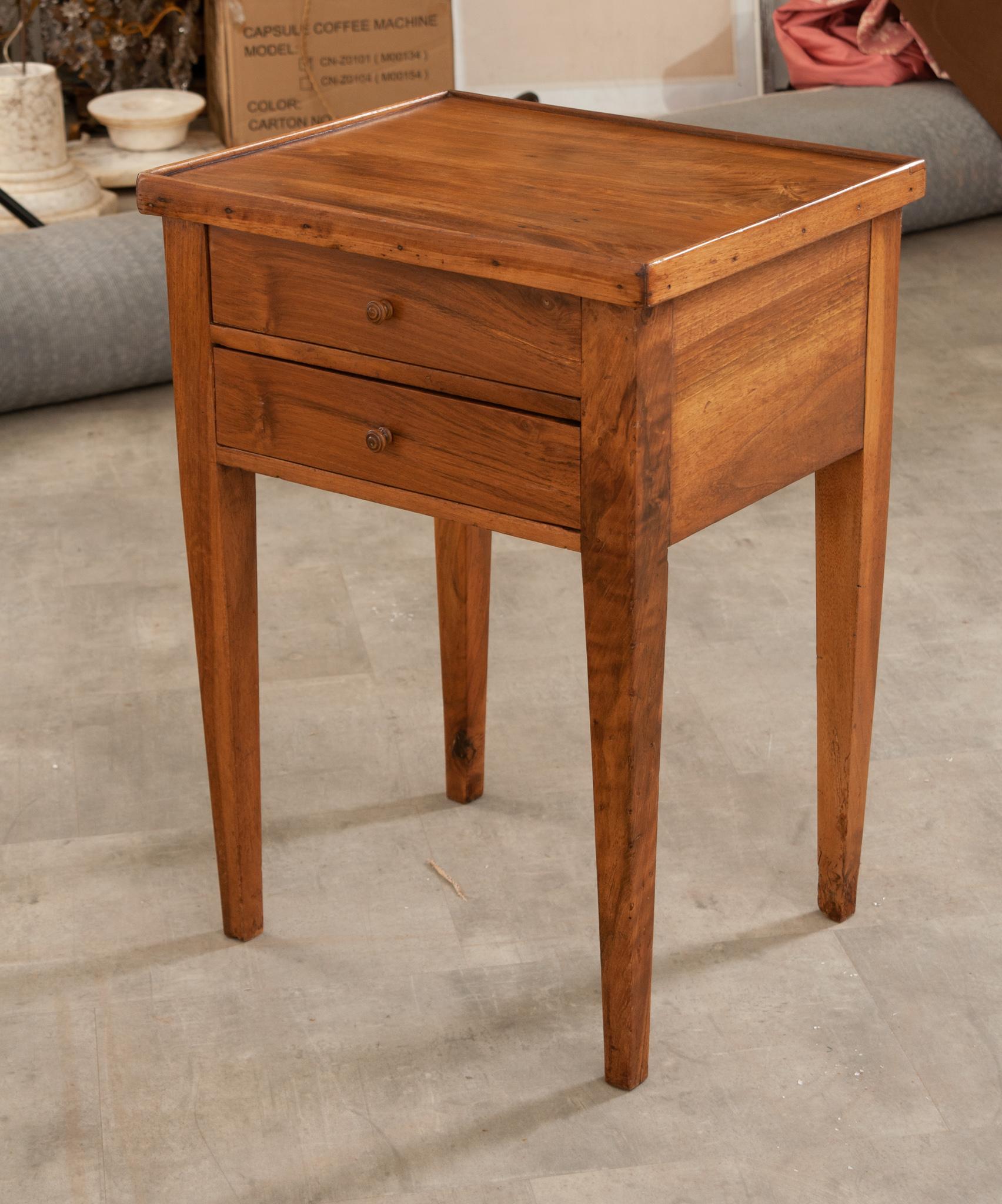 A mid 19th Century bedside table, handmade in France. This table is constructed from solid walnut and features a smooth walnut top above two drawers with tapered legs. Gorgeous graining and patina are found throughout this solid wood table. Cleaned