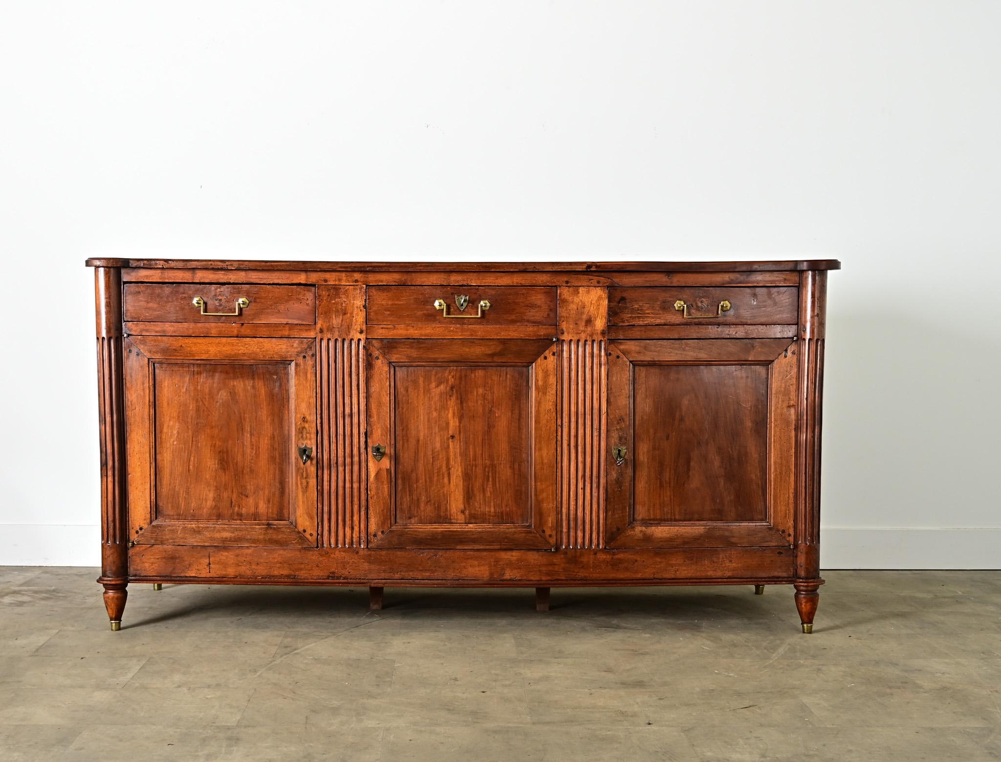 Un'intrigante enfilade in noce francese del XIX secolo, di stile più transitorio che neoclassico, che fonde gli elementi regali di Luigi XVI con il calore e la patina della costruzione provinciale. Con una forma ad angoli turriti, le tavole lisce