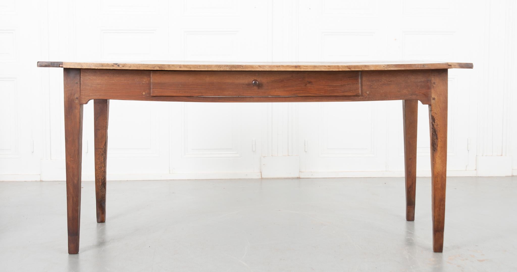 This solid walnut farm table is from 19th century France. The top is constructed with four planks of beautiful walnut, smoothed with a French wax paste. A single drawer is housed in the simple apron and fixed with a turned wooden pull. The whole is