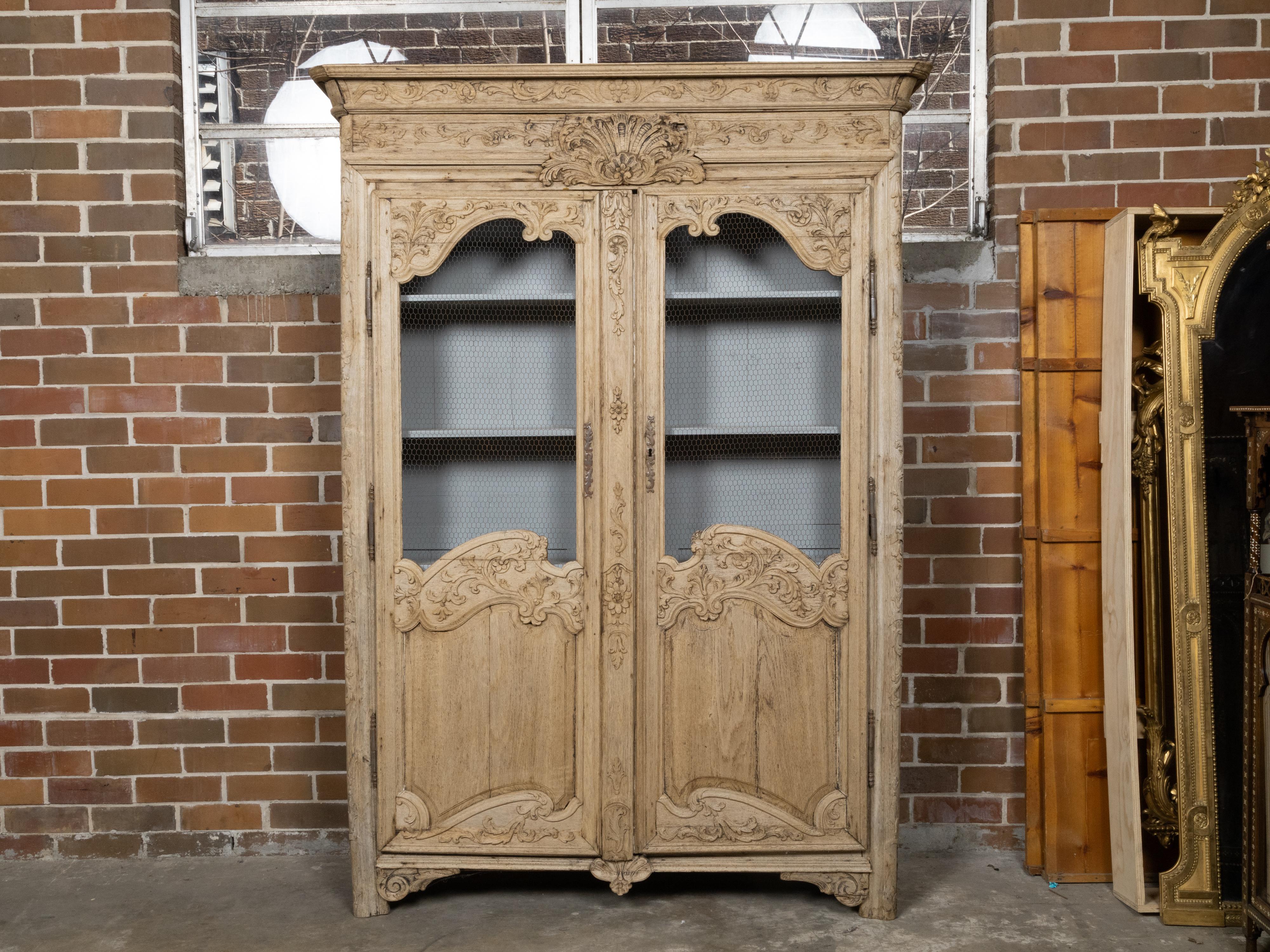 A Country French stripped wood bookcase from the 19th century with abundant carved scrolling décor, foliage and chicken wire doors. This 19th-century Country French bookcase is a magnificent piece, beautifully crafted with stripped wood that