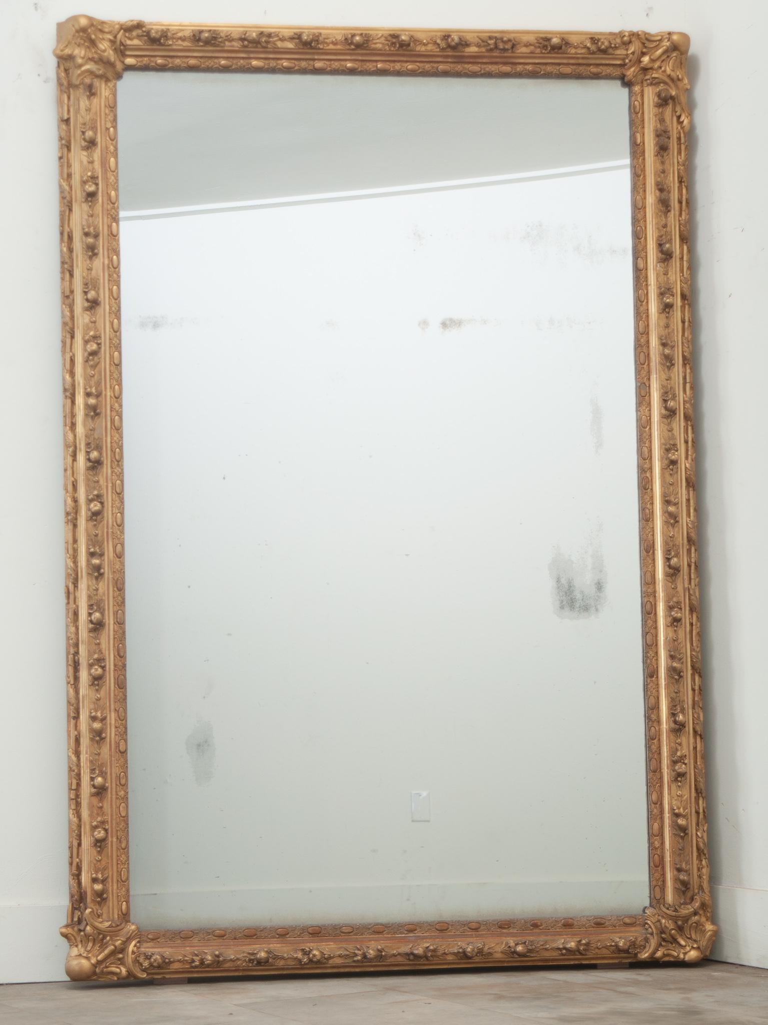 Ein symmetrischer Spiegel aus geformtem und vergoldetem französischem Holz. Dieser Spiegel hat beeindruckende Formen von Früchten, Blumen, verschlungenen Lorbeerblättern und anderen klassischen französischen Motiven, die ihn zu einem umwerfenden