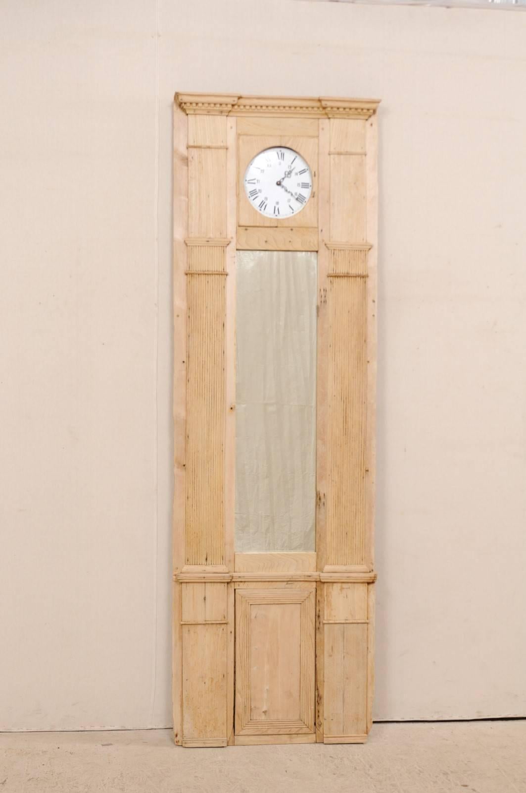 A French 19th century architectural wood panel with clock face. This antique French natural wood panel features a slightly projected cornice with dentil molding atop a clock face, inset into a panel. There is a vertical, rectangular-shaped mirror at