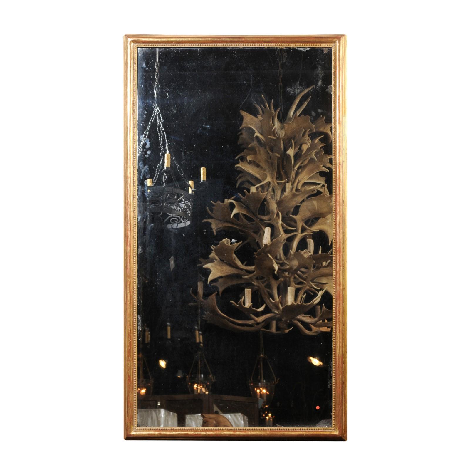 A tall French giltwood rectangular mirror from the 19th century, with beaded motifs and original mercury glass. This French giltwood mirror features an elegant linear silhouette, simply adorned with a molded frame, accented on the inside with