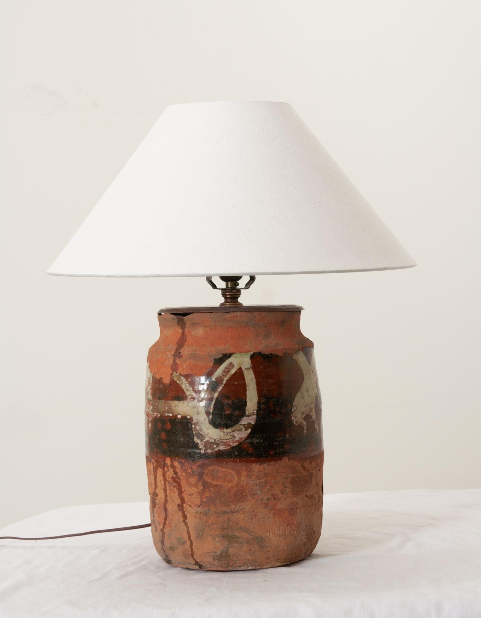 A wonderful terracotta vessel from France once used as an olive jar now upcycled into a table lamp featuring a uniquely patterned glaze finish and modern linen shade. Newly wired in the USA with all UL approved parts and topped with patinated brass.