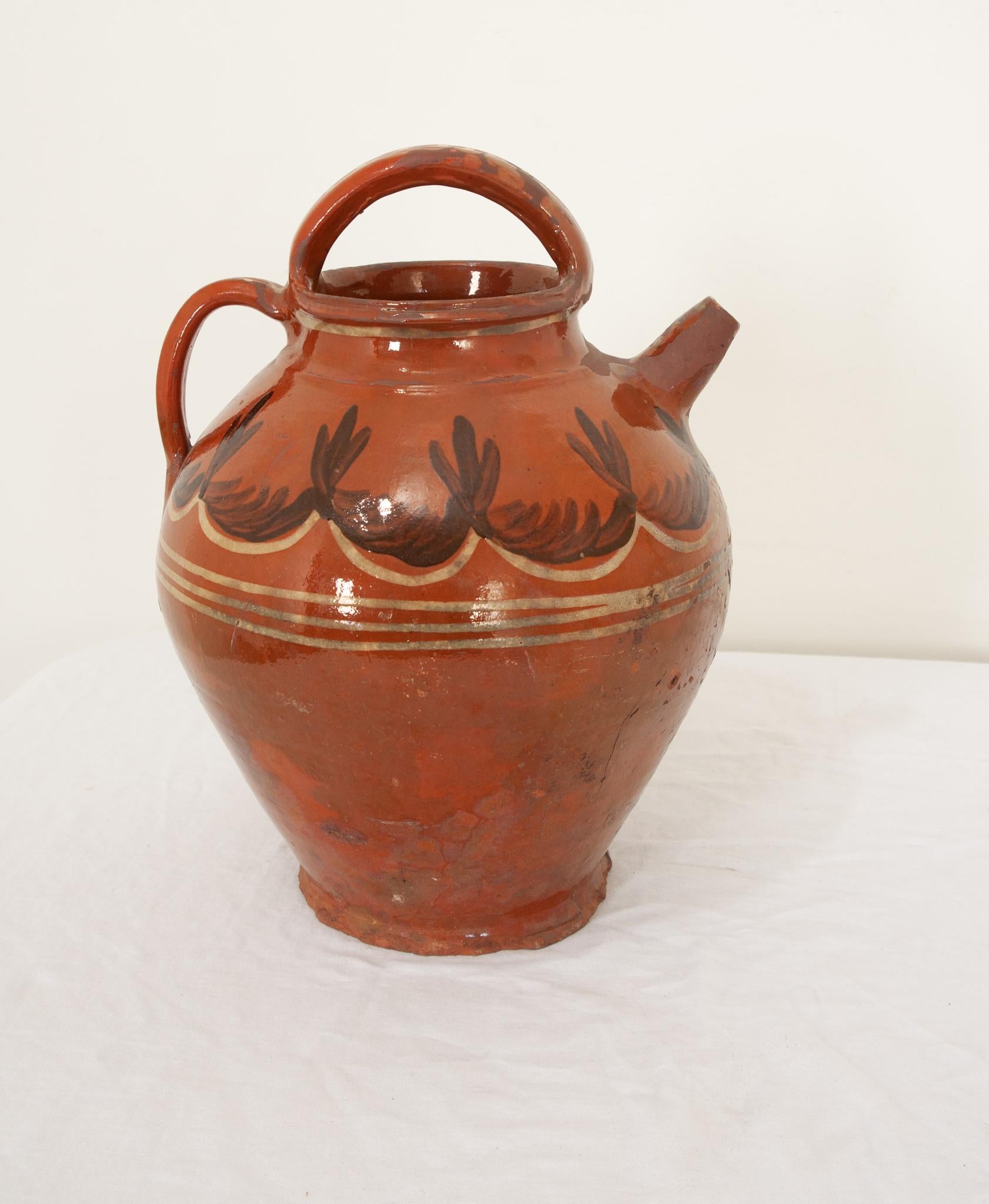 A French terracotta olive oil jar from the 19th century, with wonderful glazes of vibrant orange and detailed cream and black decorations of fluid lines and surrounding foliate designs. Hand-crafted in France circa 1850 this terracotta oil jar has a