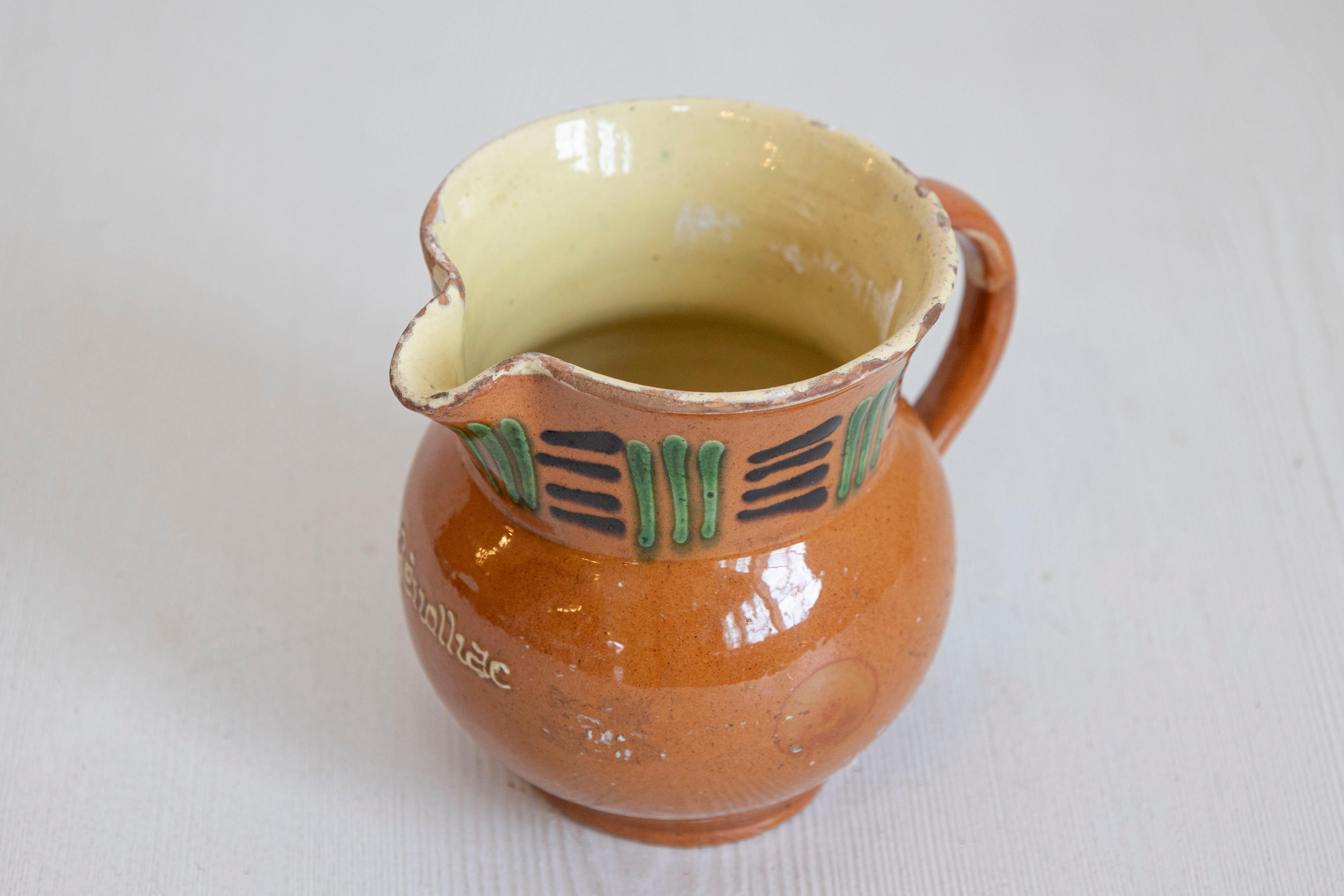 Pichet en terre cuite de Génolhac, datant du 19e siècle, avec une glaçure rousse et des accents verts et noirs. Créé dans le sud de la France au cours du XIXe siècle, ce pichet rustique présente un fond de couleur roussâtre accentué par de simples