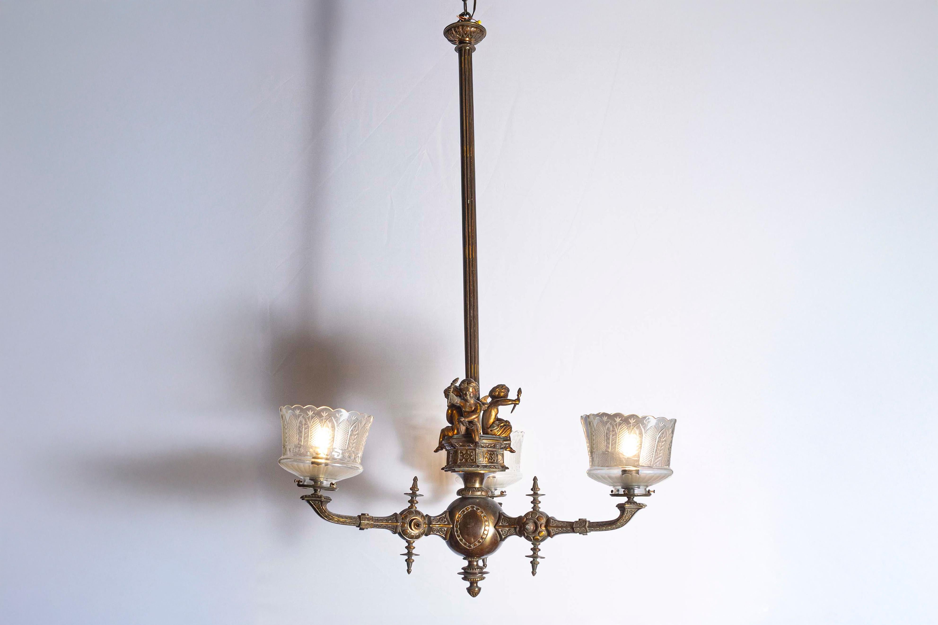 Lustre français à trois lumières en bronze du XIXe siècle, avec des chérubins tenant des torches et des abat-jours en cristal de Baccarat. Né en France à l'époque du dynamisme politique du XIXe siècle, cet élégant lustre présente une fine baguette