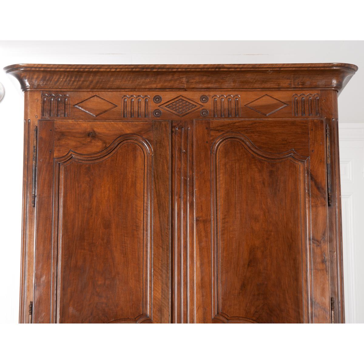 An absolutely stunning hand-carved, hand-pegged walnut armoire. A large Louis Philippe-style crown cornice sits just above a carved Directoire-style frieze. Two large, Louis XV-style shaped doors equipped with a working lock and latch are hung on