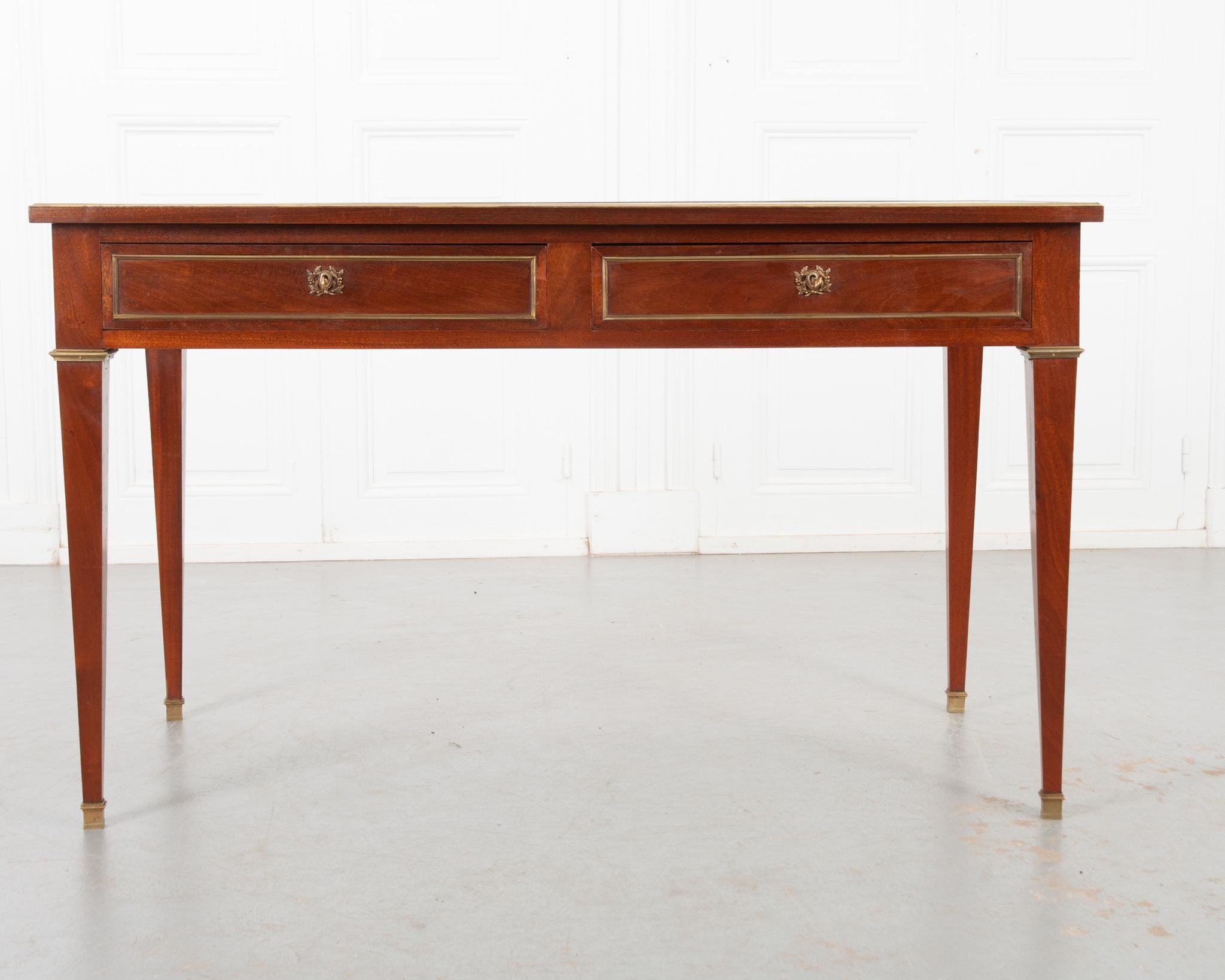 A studious transitional style desk from France, circa 1850. Writing surface and slides inset with caramel toned leather. Wear is consistent with age and use. A thick brass band encircles the edge of the top. With both slides out the maximum width is