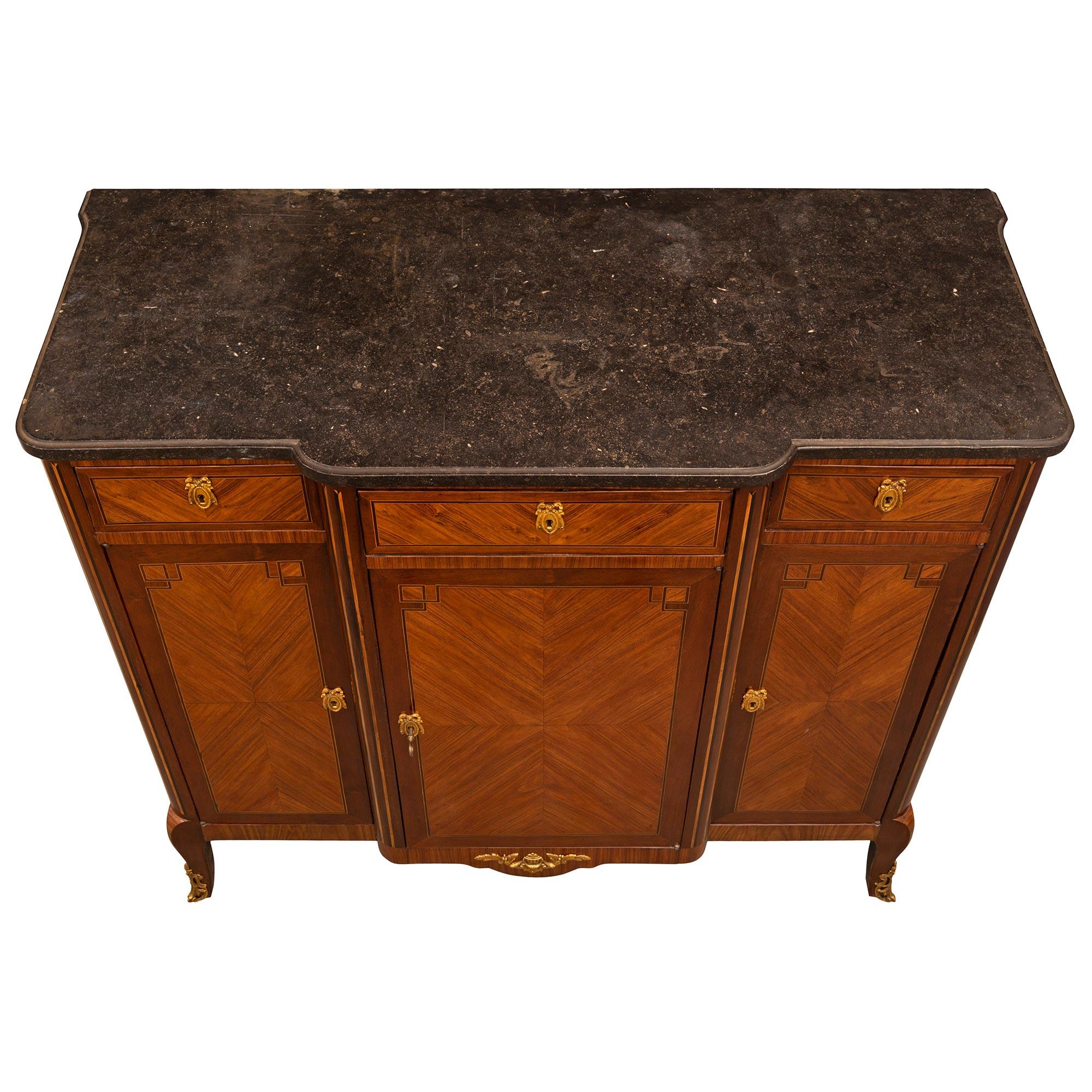 An elegant French 19th century Transitional st. Tulipwood, Kingwood, ormolu, and Black Belgian marble buffet. The three door three drawer buffet is raised by cabriole legs with fine pierced foliate ormolu sabots below the frieze which is centered by