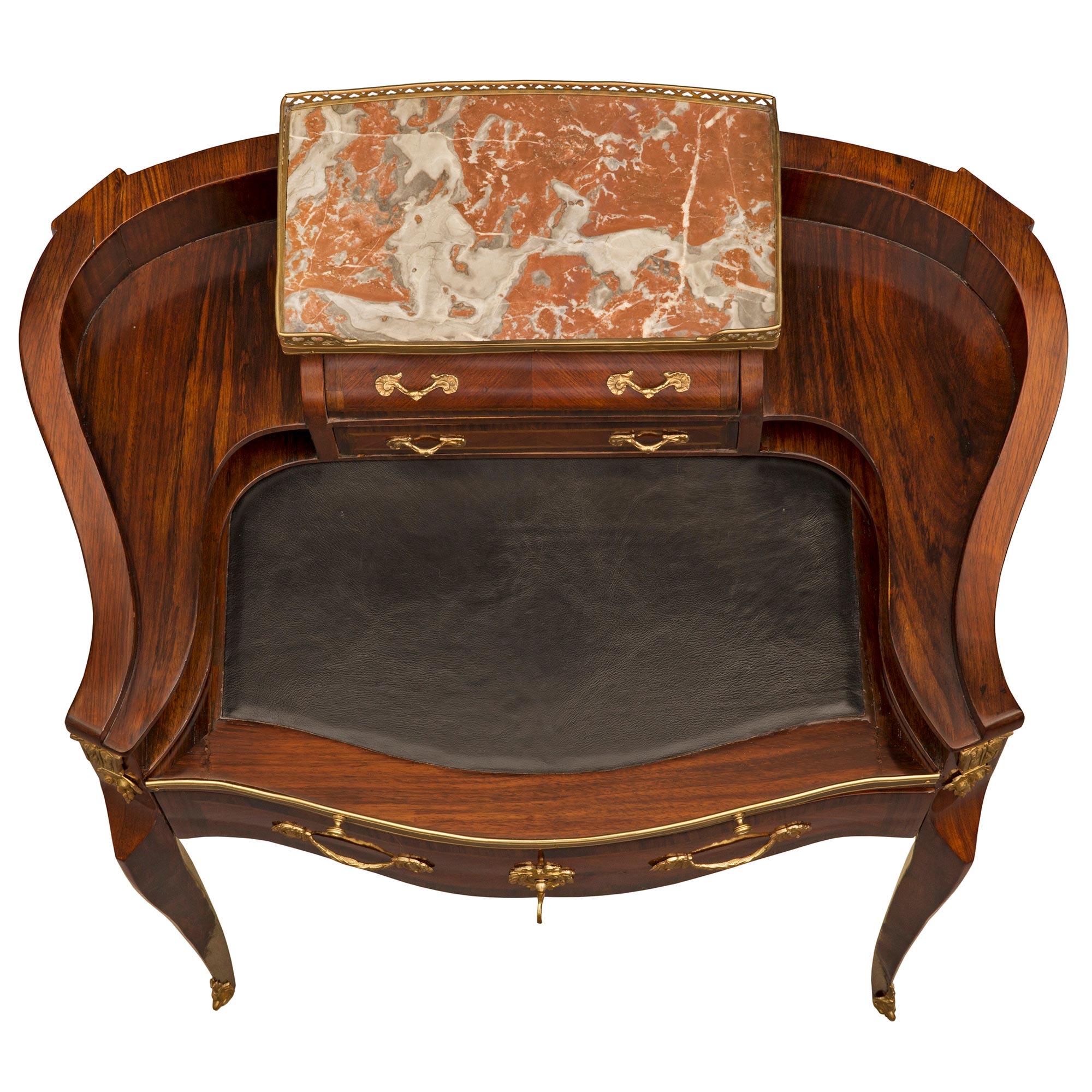 An elegant French 19th century Louis XV st. Rosewood, Kingwood, Tulipwood, ormolu, and Incarnat Turquin marble desk. The three drawer desk is raised by slender cabriole legs with fine foliate ormolu sabots. The bombee scallop shaped apron displays