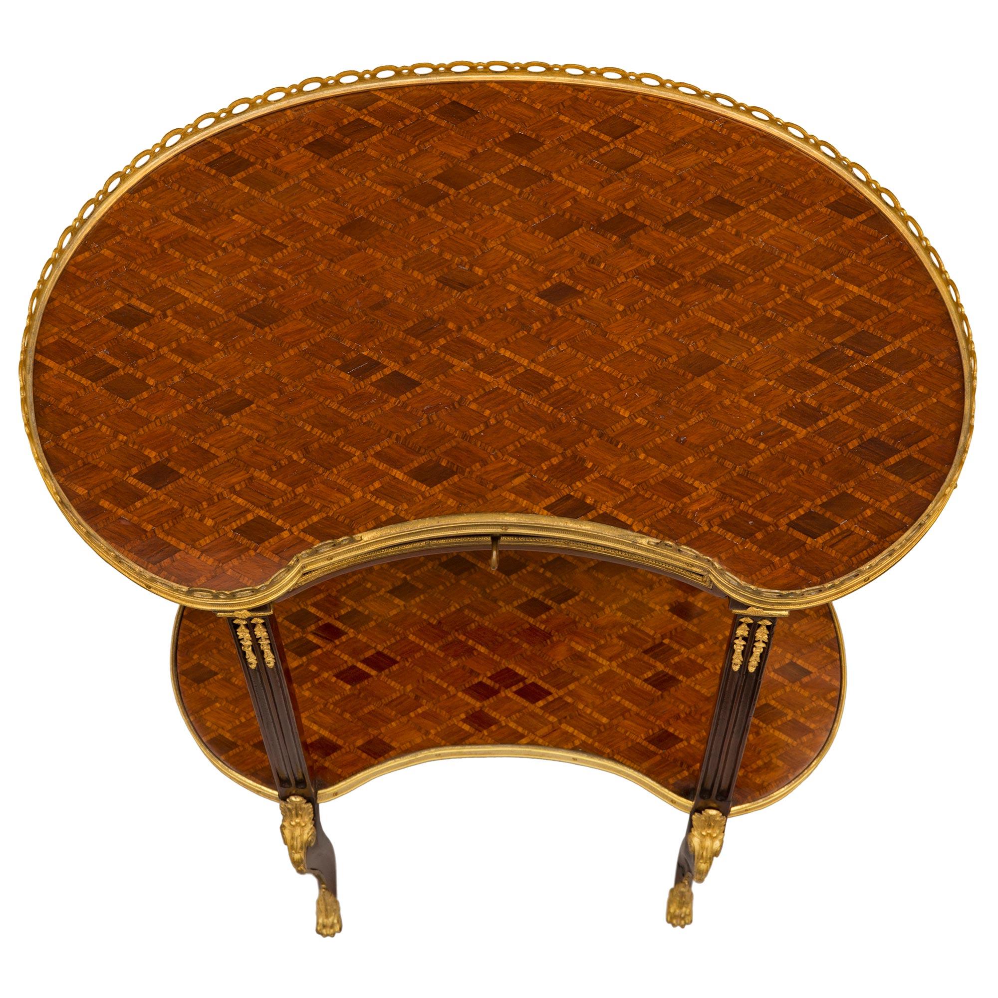 An exquisite French 19th century Transitional st. Mahogany, Kingwood, and ormolu side table. The two tiered kidney shaped table is raised by delicately scrolled legs with richly chased ormolu paw shaped feet and a charming tapered chute leading to
