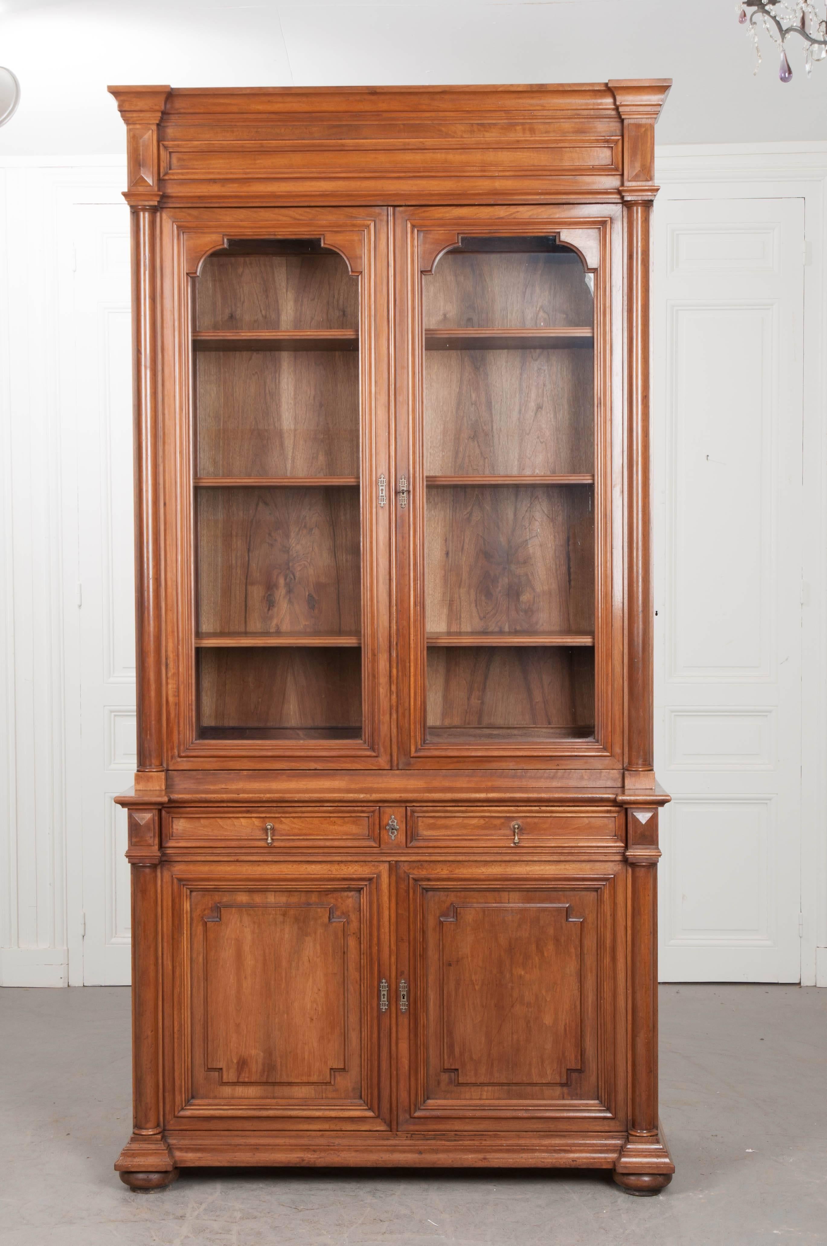 An extraordinary walnut bibliothèque, made in France, circa 1880. This wonderful case piece combines styling elements from both the Louis XIII and Louis Philippe periods. The upper cabinet has two glass-front doors that lock before a shelved