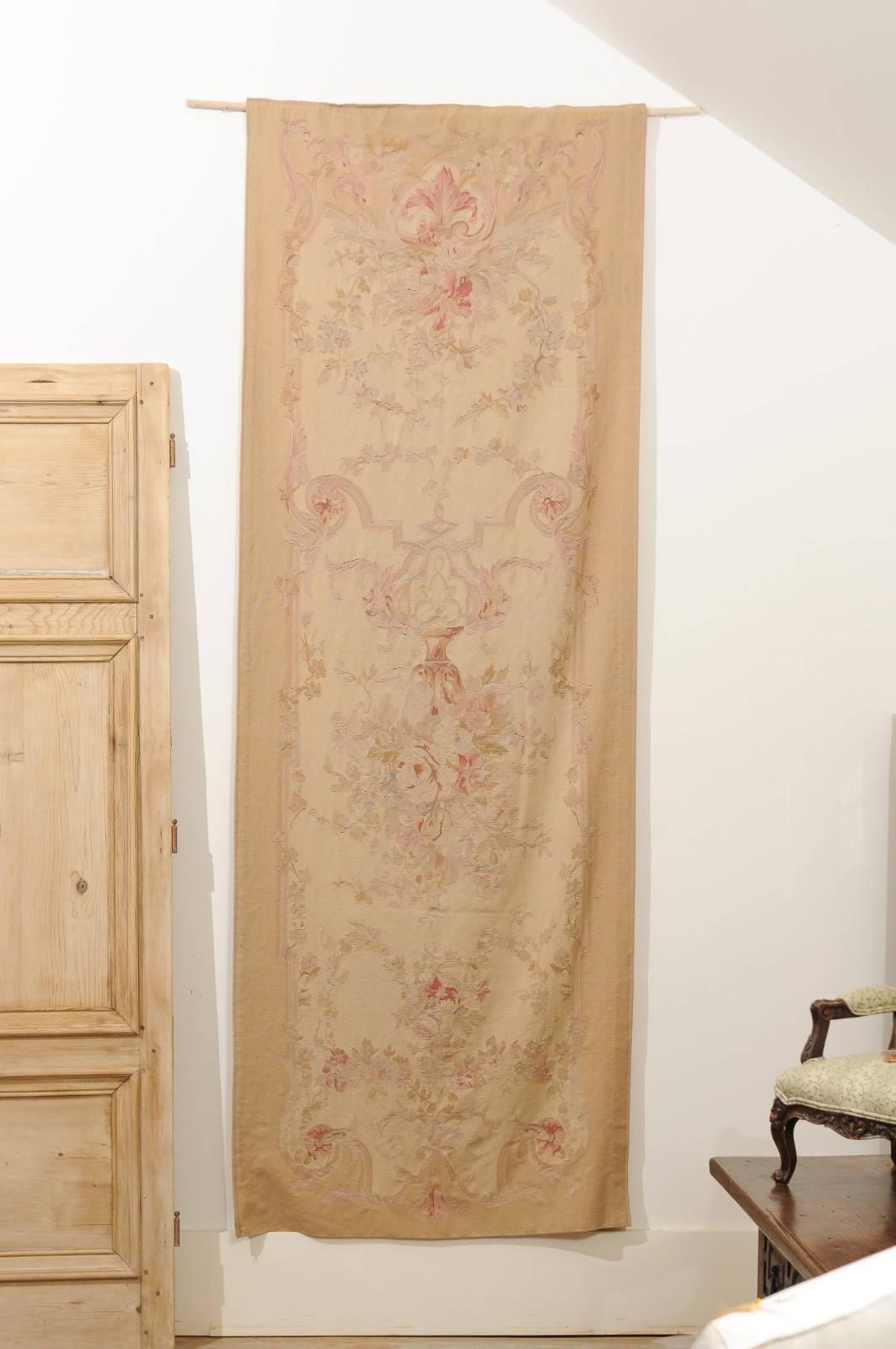 A French handwoven vertical tapestry from the 19th century, with soft muted colors and floral décor, lined and backed with a hanging sleeve. This exquisite French tapestry features a tall Silhouette, beautifully adorned with floral motifs standing