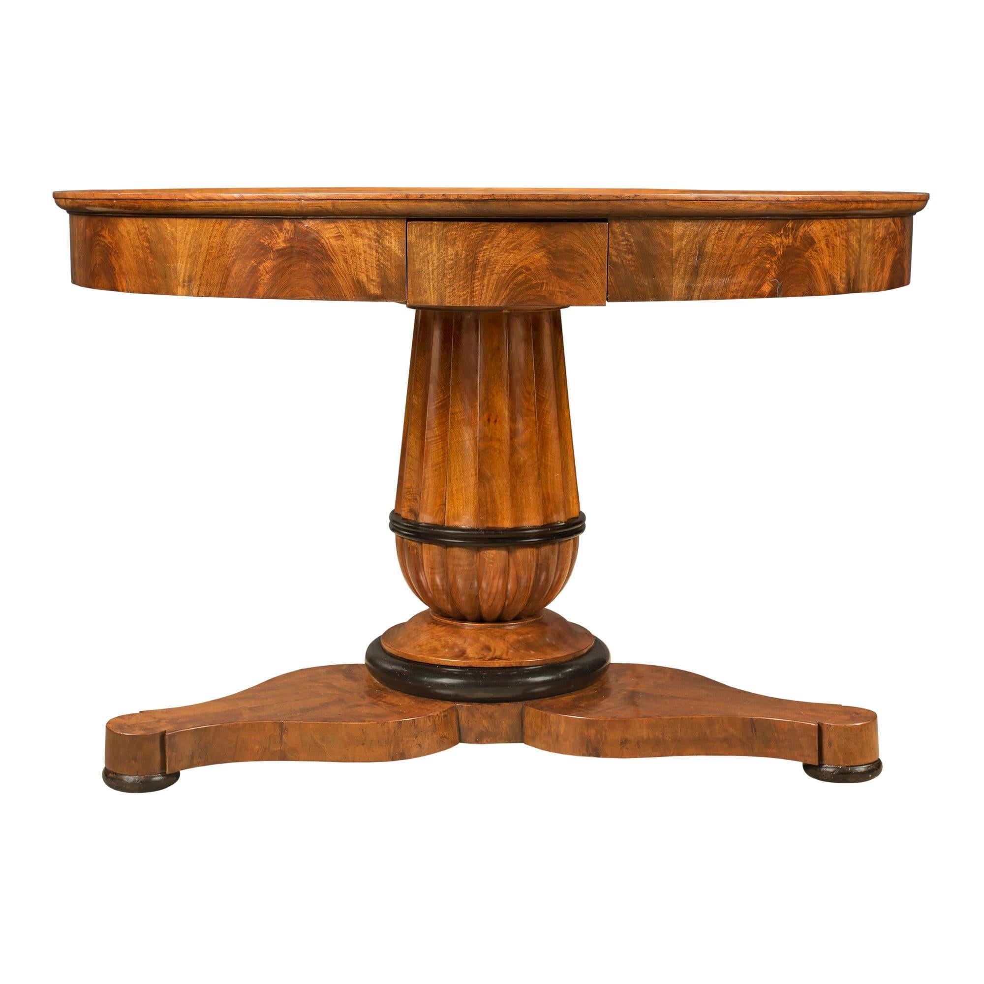 A handsome French 19th century walnut and ebonized fruitwood circular center table. The table is raised by a triangular base with finely scalloped shaped sides and ebonized fruitwood bun feet. The central support displays a most decorative fluted