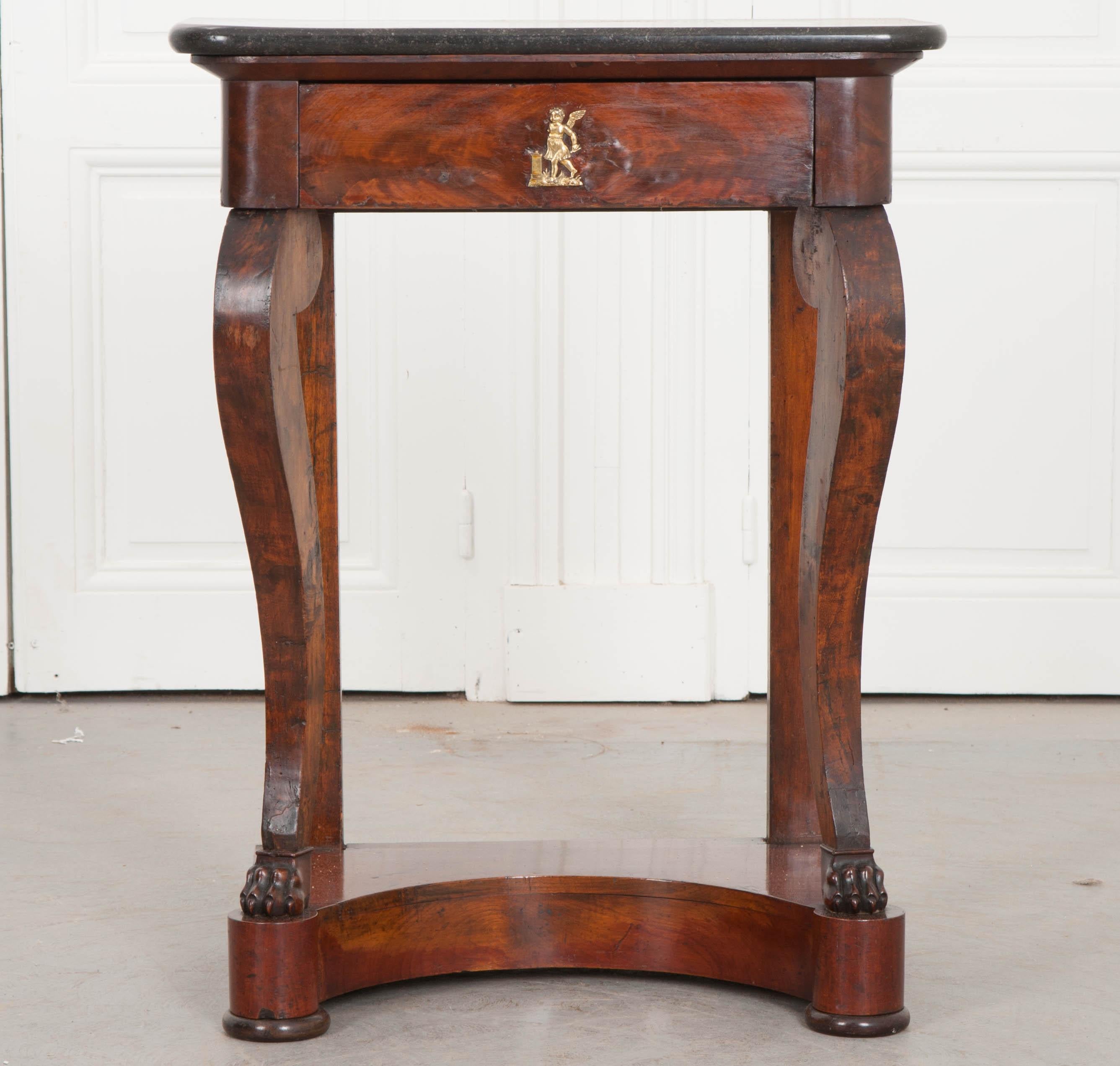 A petite mahogany and walnut console from the Restauration period in early 19th century France. The table is topped in a lovely piece of black fossil marble that has rounded front corners to match the base. The apron has a single drawer with brass