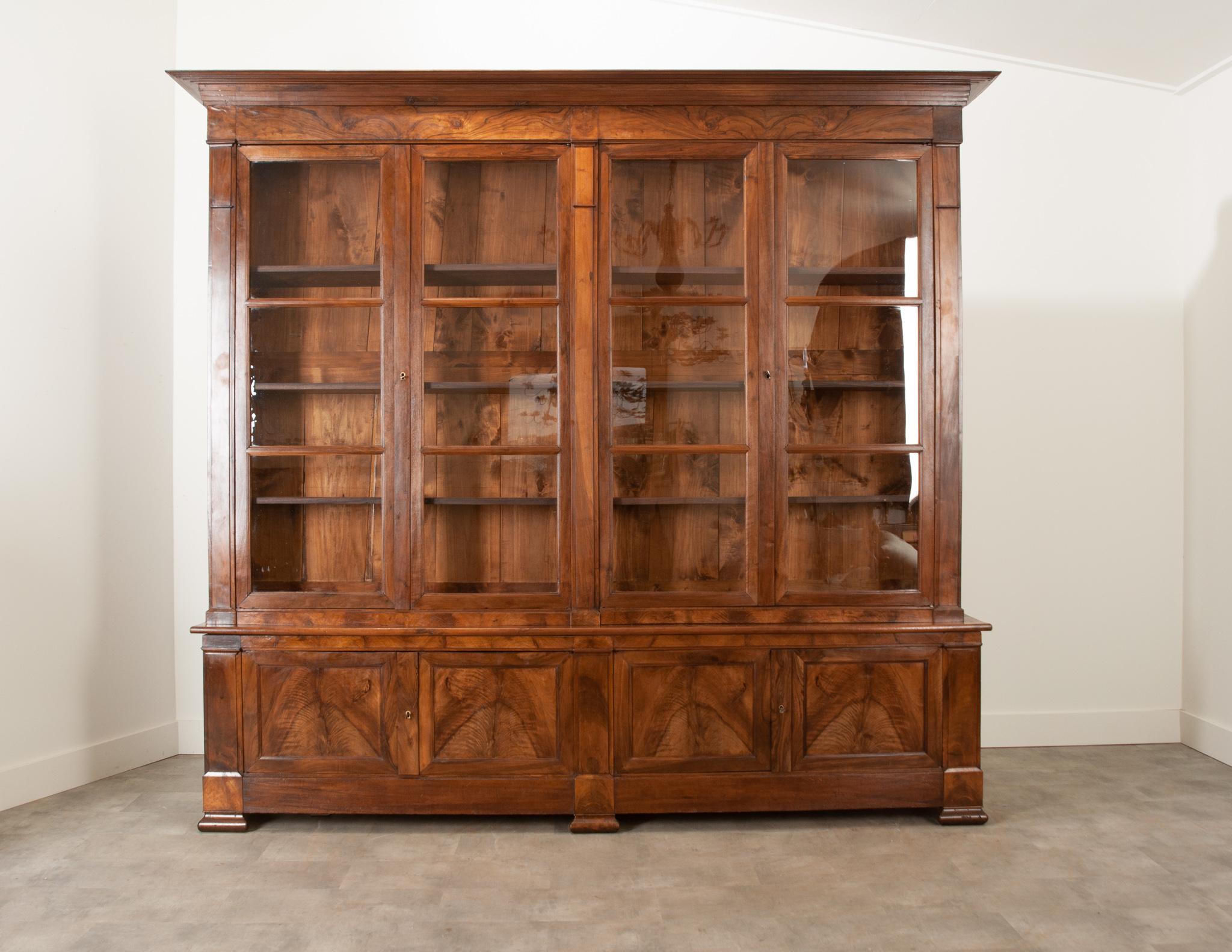 This large Louis Philippe bibliotheque is a magnificent way to display or store any precious decor items in your home or office. Unlocking the four glass front doors reveals a single interior cavity with three dovetail adjustable shelves. The lower