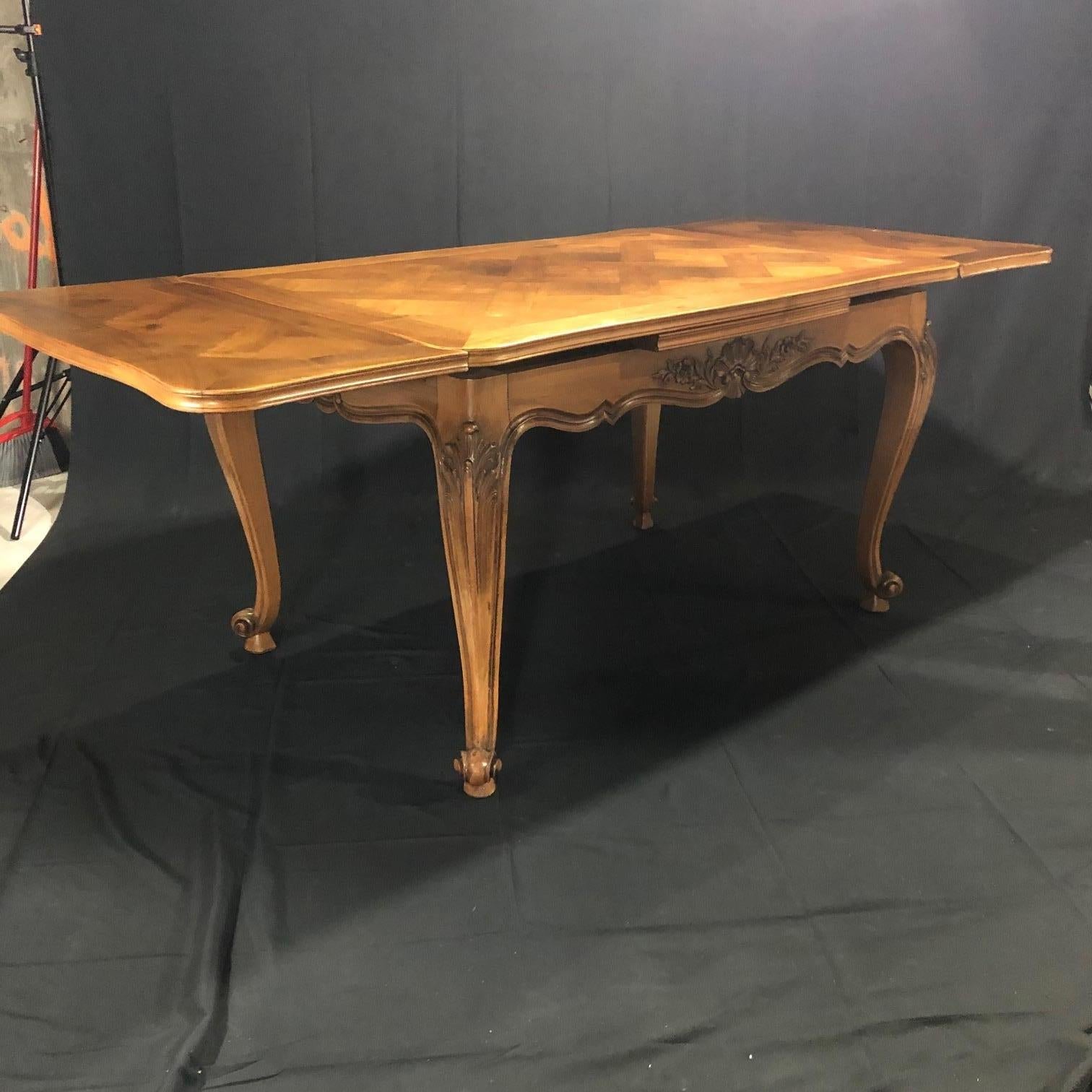 Spectacular carved French 19th century walnut country parquet inlay dining table with two draw leaves having wonderfully hand carved and scalloped apron with scrolls and flower baskets, cabriole legs with carved decorated acanthus leaves and