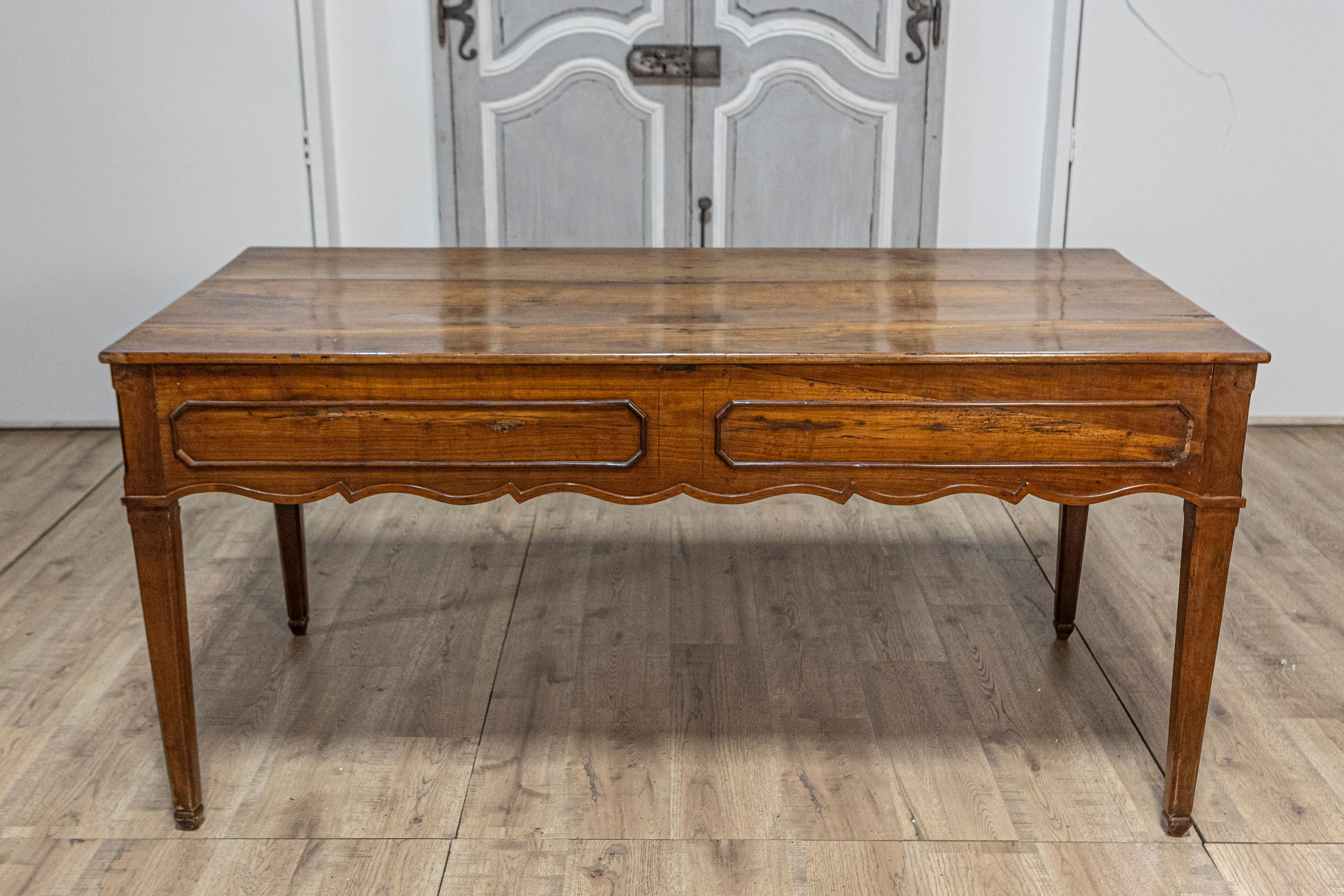 A French walnut desk from the 19th century with carved apron and lateral drawer. This elegant French walnut desk from the 19th century is a splendid example of classic craftsmanship, combining functional design with ornate aesthetic details. The