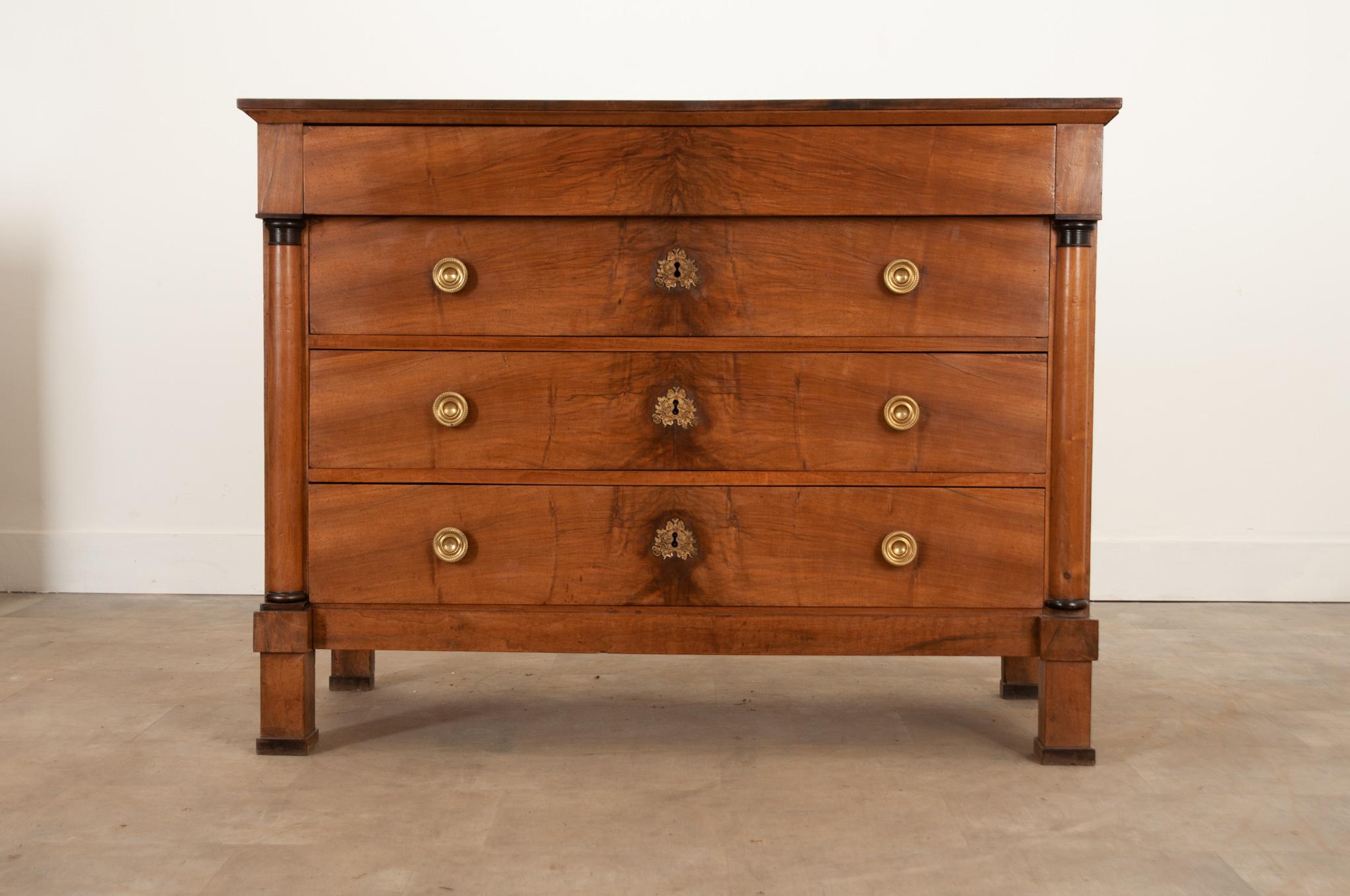 A handsome bookmatched walnut commode from France crafted during the 1830s. Composed in the Empire style. The apron houses a hidden drawer above a bank of three equally sized drawers below. Each drawer front is fixed with a pair of lustrous circular