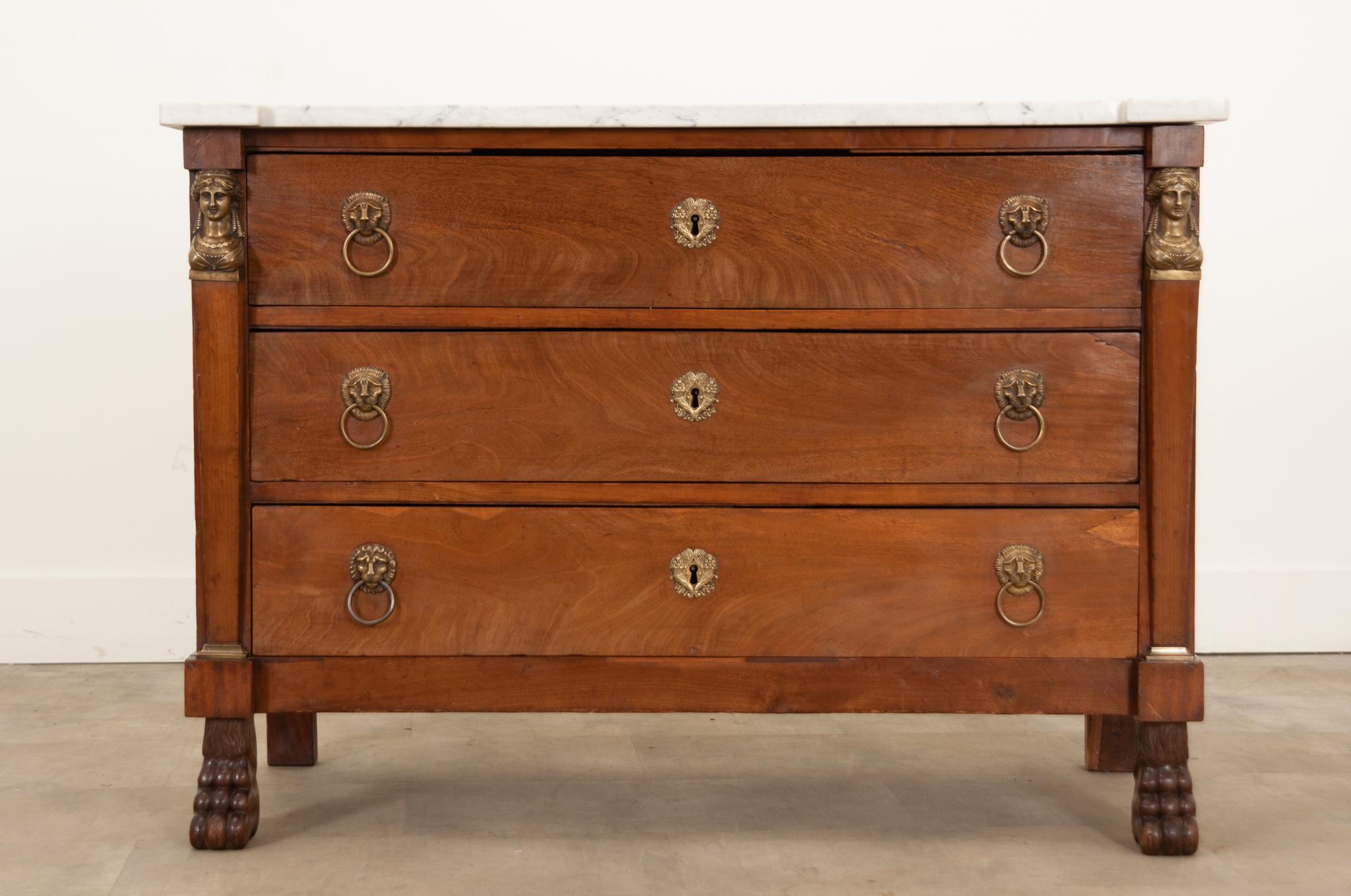 A wonderful French walnut commode hand-crafted in France circa 1830 with rather grand Empire style elements. Topped with a removable piece of white marble with lovely gray veining and shaped front corners. Three long drawers have matching cast brass