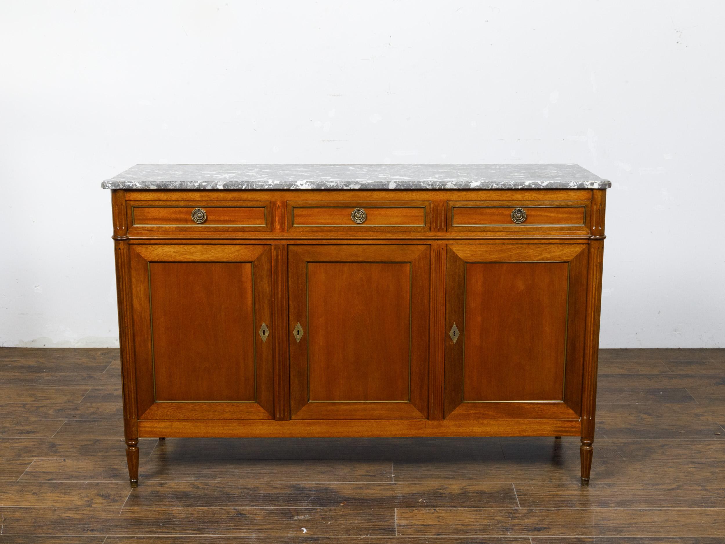 A French Louis XVI style walnut enfilade from the 19th century with gray marble top, three drawers over three doors. This French Louis XVI style walnut enfilade from the 19th century is crowned with a beautiful variegated gray marble top, featuring