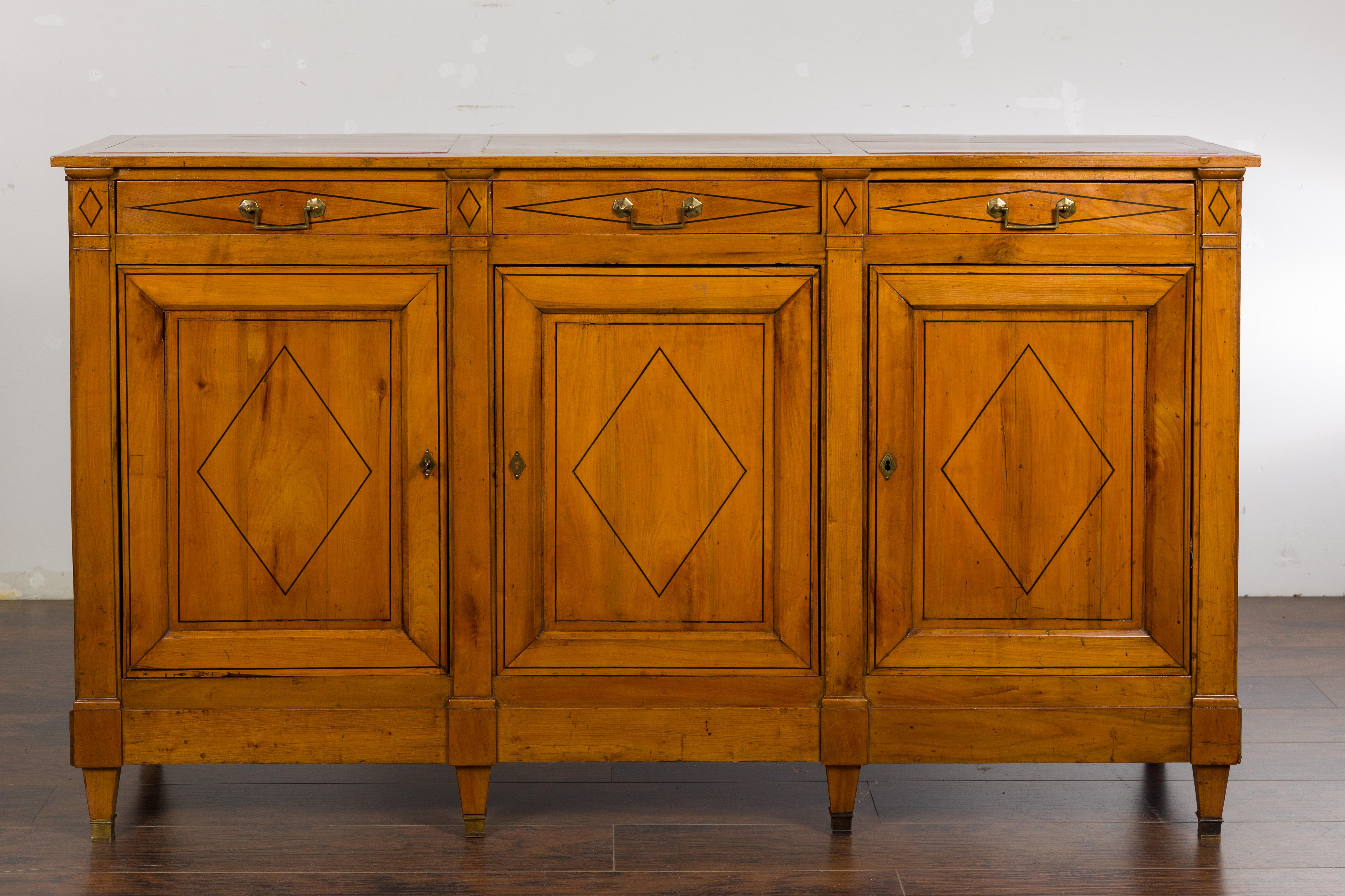 A French walnut enfilade from the 19th century with three drawers over three doors, black inlaid diamond motifs, brass hardware and tapered feet. Introduce a touch of French elegance to your living space with this exquisite walnut enfilade from the