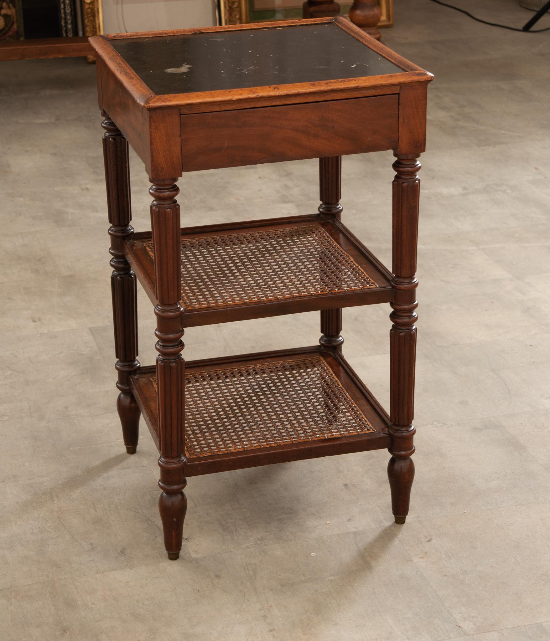 An elegant 19th century French etagere hand-crafted in Burgundy circa 1870. Built of fine walnut, this square table stands on finely turned and fluted baluster legs ending with arrow feet. Connected at the base are two cane shelves over a straight