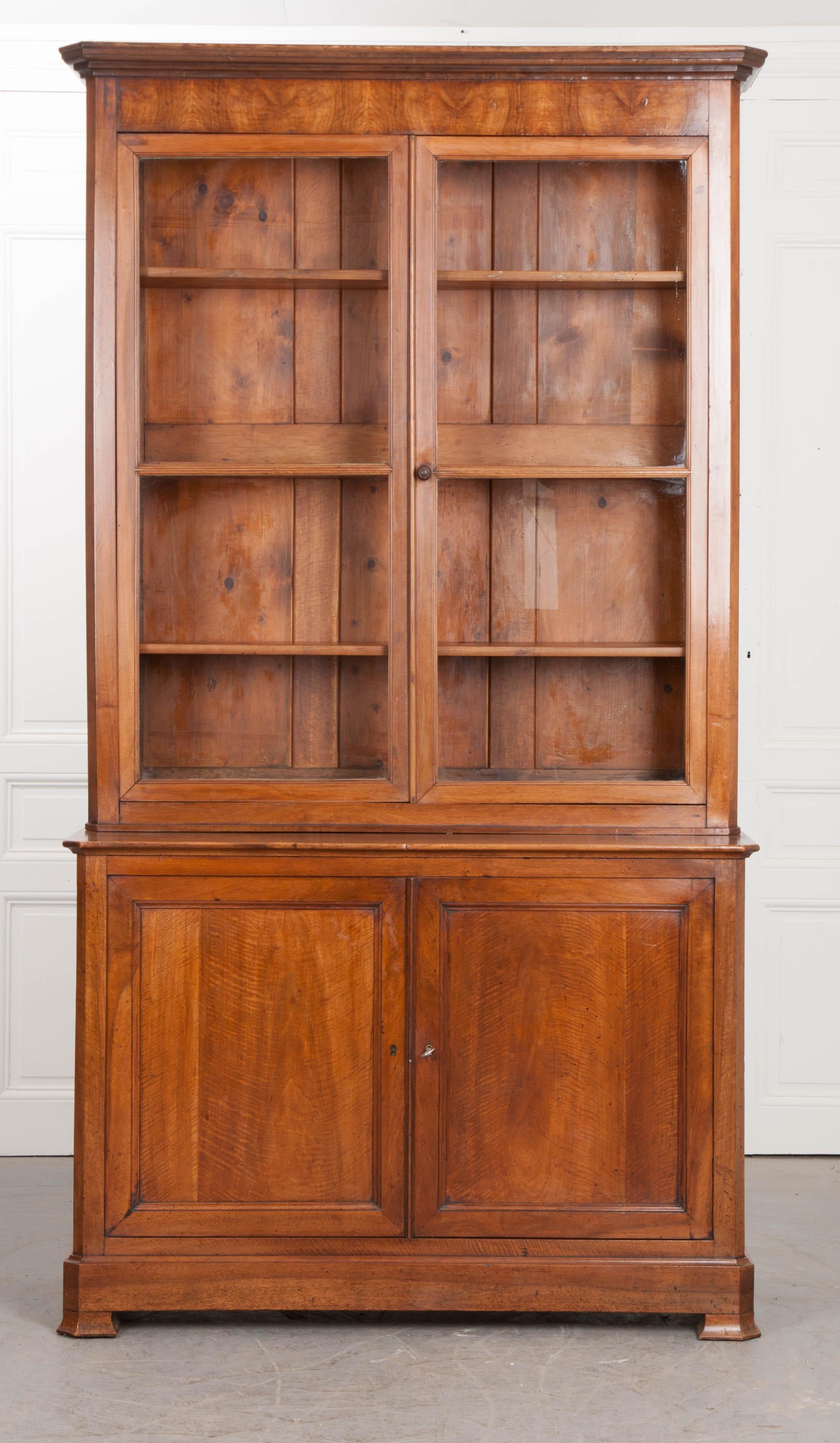 An impressive walnut bibliothèque, in the Louis Philippe style, from France, c. 1880's. This exceptional case piece stands right at 8' tall and can separate into two bodies for easier transport. The upper body is the bookcase. It is glass-front,