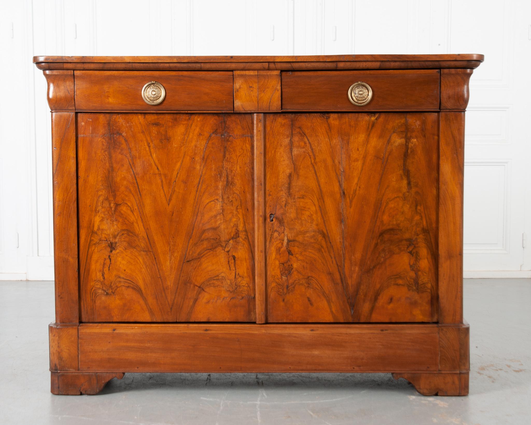 Wonderful, book matched burl walnut veneer draws the eye towards this luring Louis Philippe buffet. Made in France, circa 1880, the case antique is constructed with two drawers set above a singular interior cavity. The walnut top has rounded front