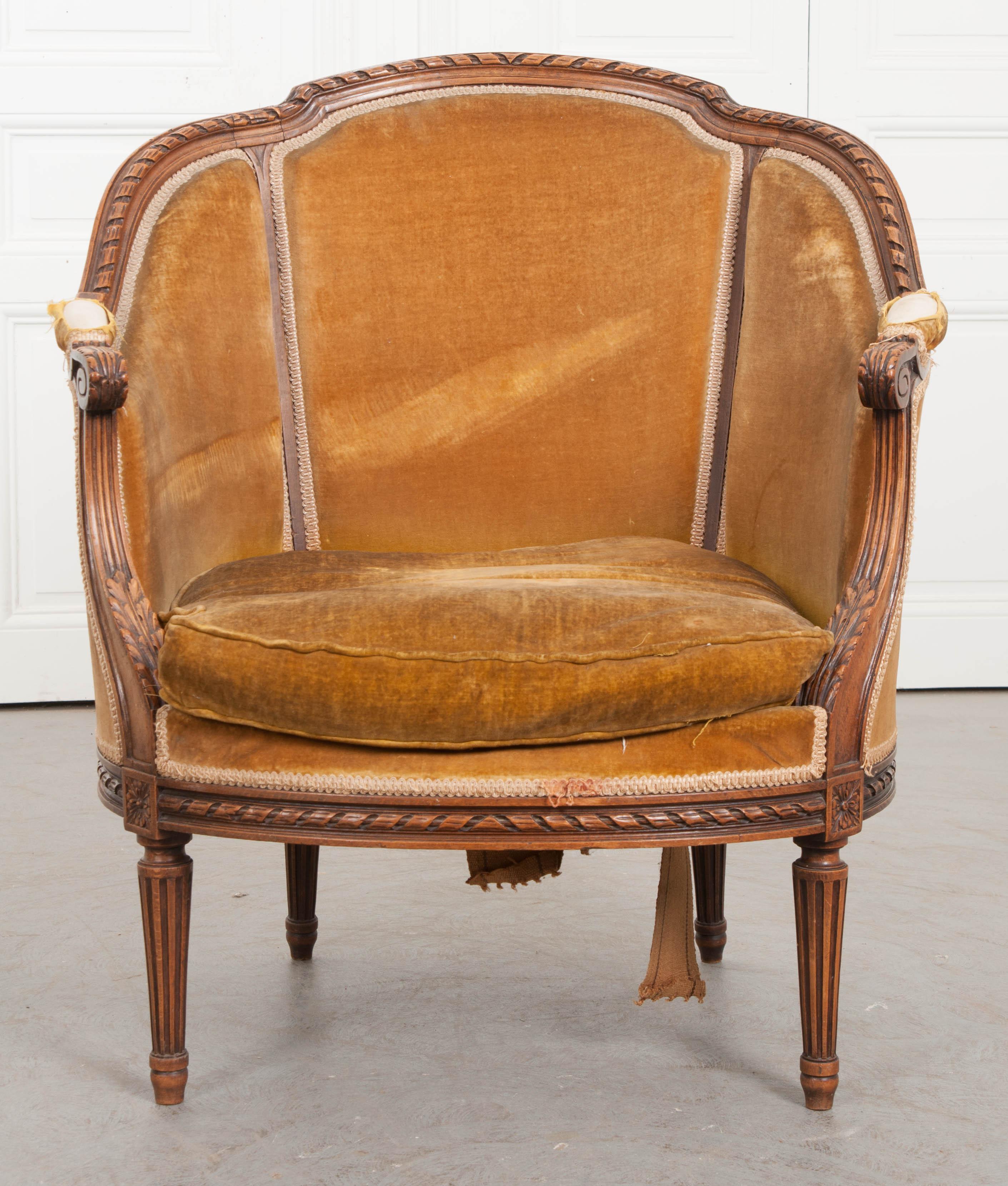 A Regal Louis XVI style bergère from 19th century, France. The bergère has a solid walnut frame that has been totally hand carved. It has a barrel shape, with a curved, shapely top rail. The top-rail, as well as apron, are trimmed in a carved