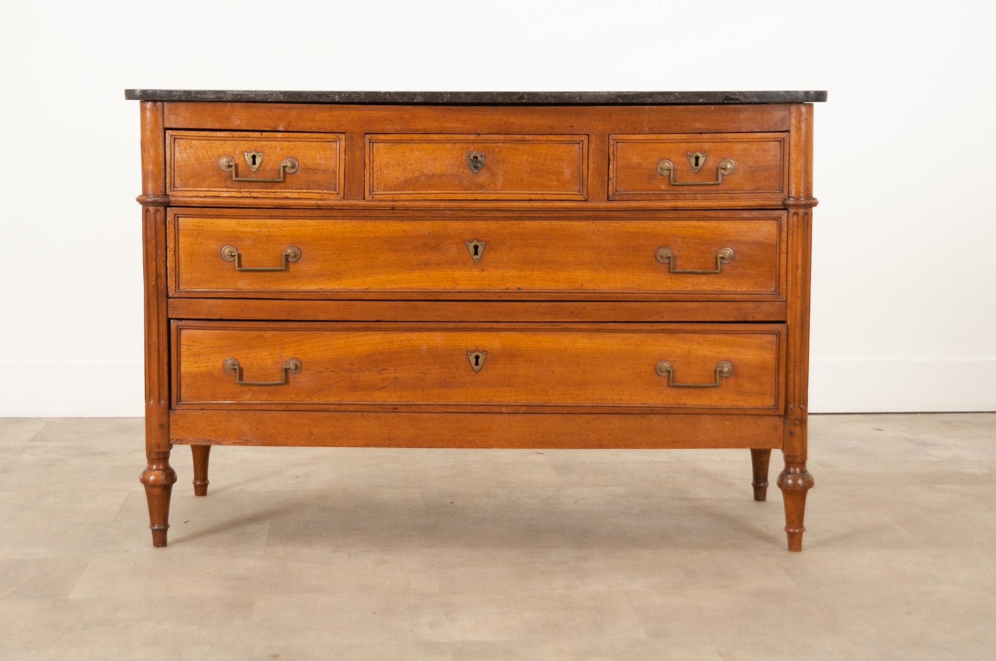 An early 19th Century French Louis XVI style commode made of beautifully toned walnut. Hand-crafted in France circa 1810, its original shaped black marble top has white and gray tiny patterns that resemble the night sky, and it sits over five