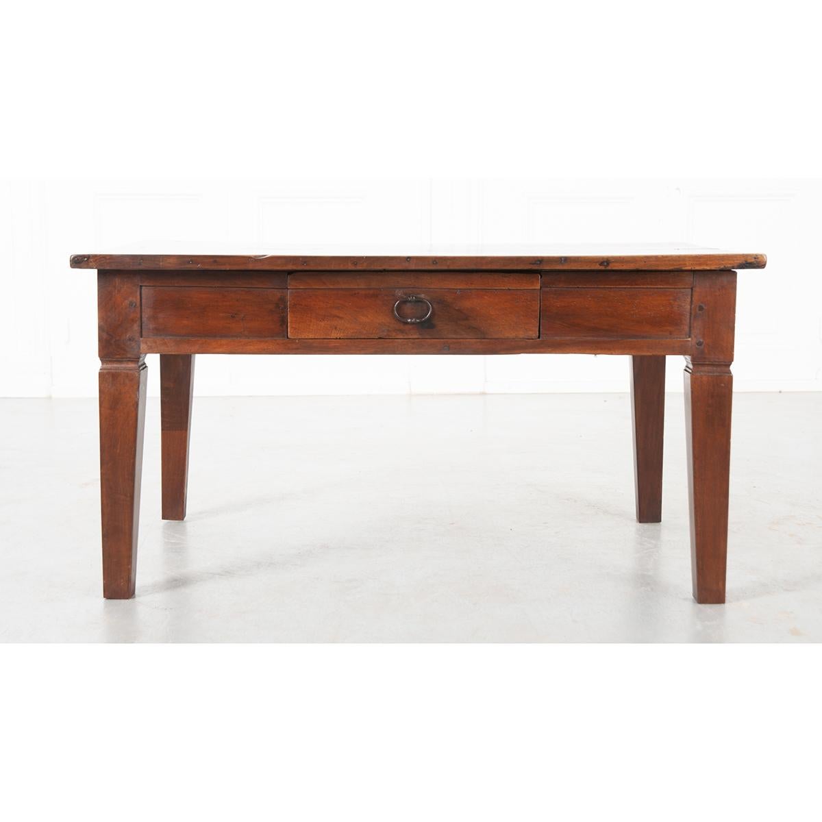 This is a French 19th century walnut low table. It is circa 1840 and put together with wood pegs. The top is made of two wide boards sitting over an apron with a single drawer which has an iron pull. All sit on straight tapered legs with a notch