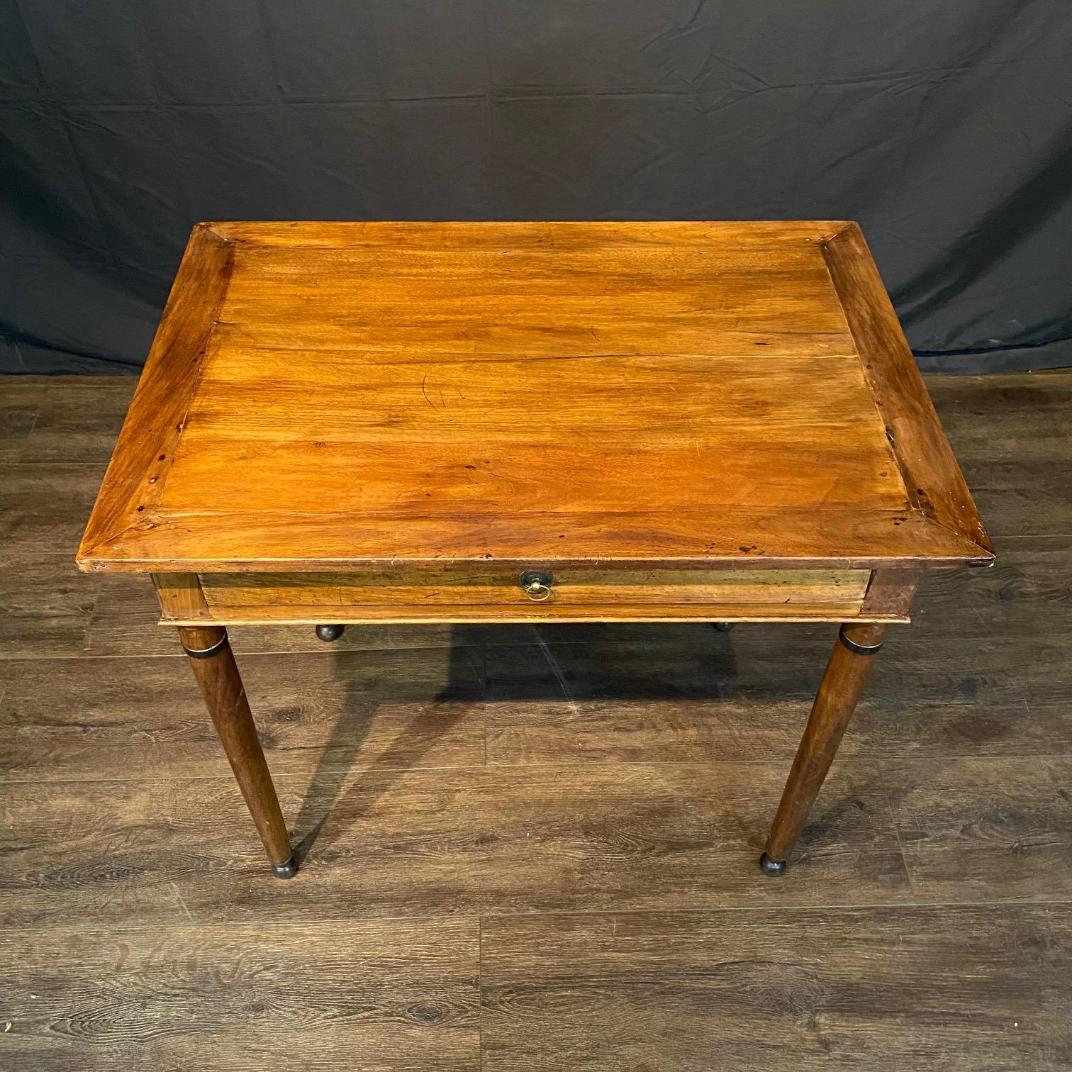 Elegant petite antique writing desk that could also be used as a side table, commonly referred to as a “bureau plat,” likely dating from the early 19th century. Crafted from a warm-toned walnut, the desk features clean and simple lines, embodying a